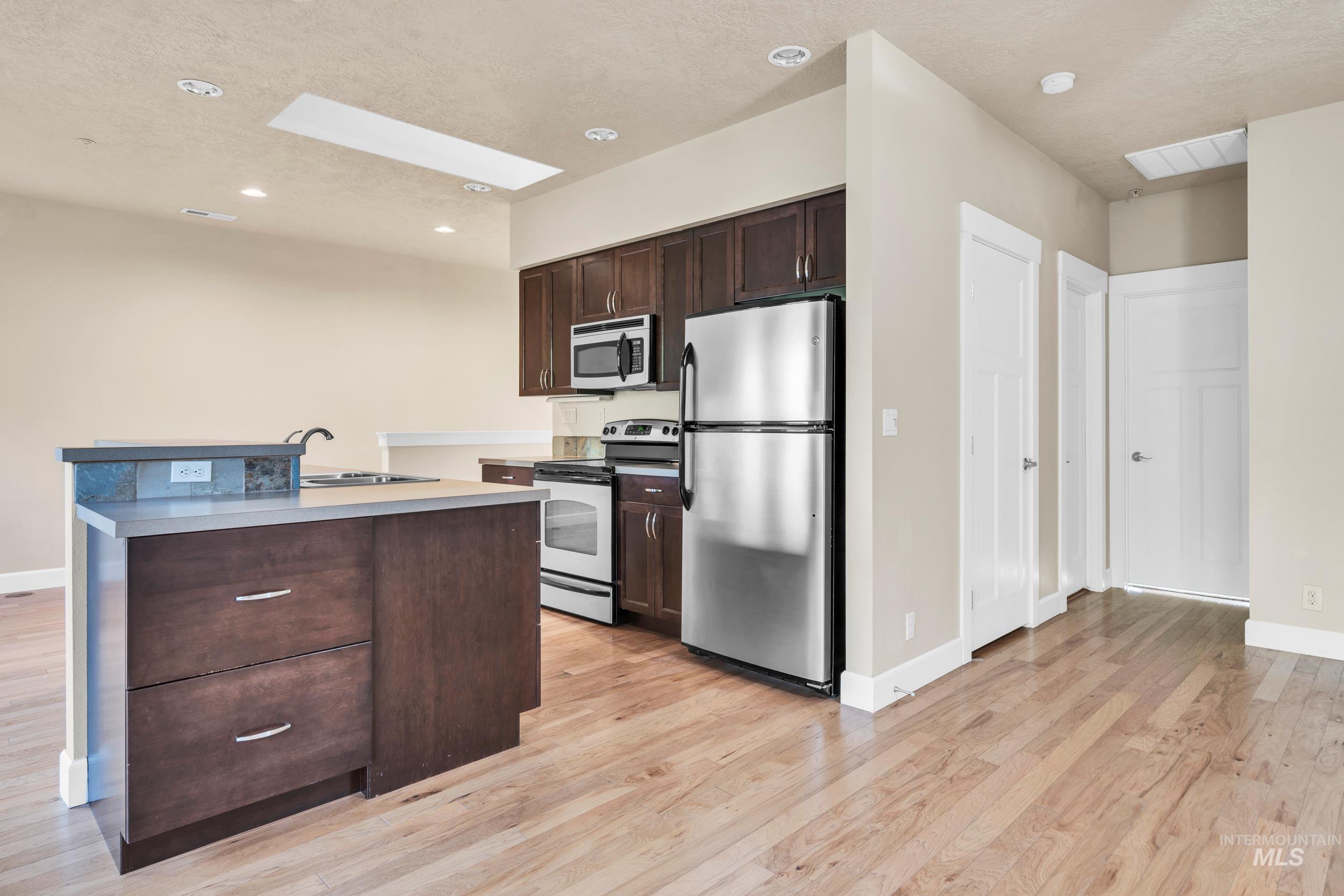 Kitchen with appliances with stainless steel finishes, dark brown cabinets, recessed lighting, a textured ceiling, and a skylight