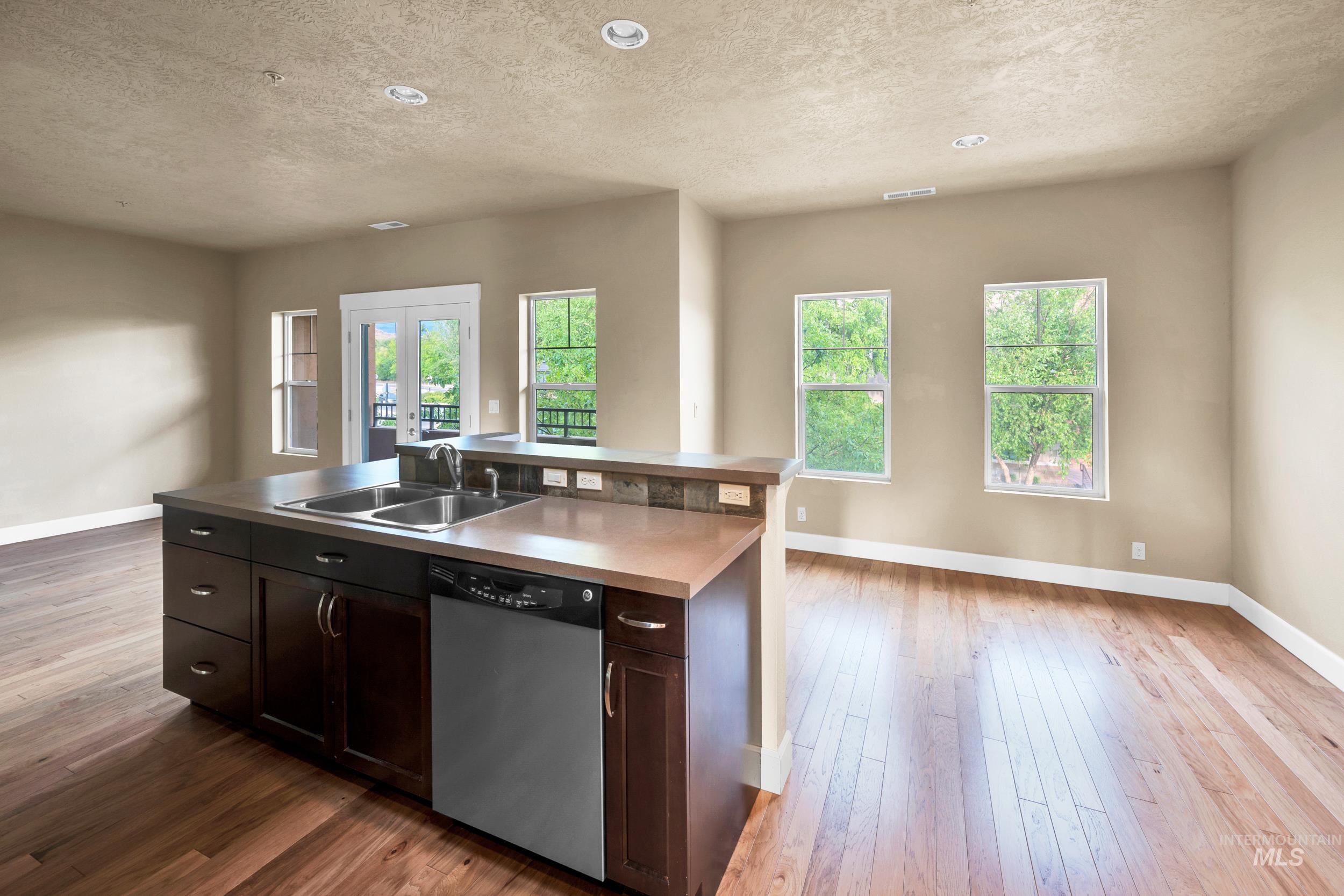 Kitchen featuring dark brown cabinets, dishwasher, a textured ceiling, a kitchen island with sink, and light wood-type flooring