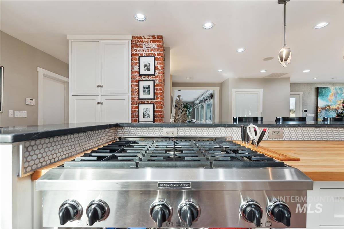 Kitchen view of pendant lighting, white cabinets, butcher block countertops, recessed lighting, and tasteful backsplash