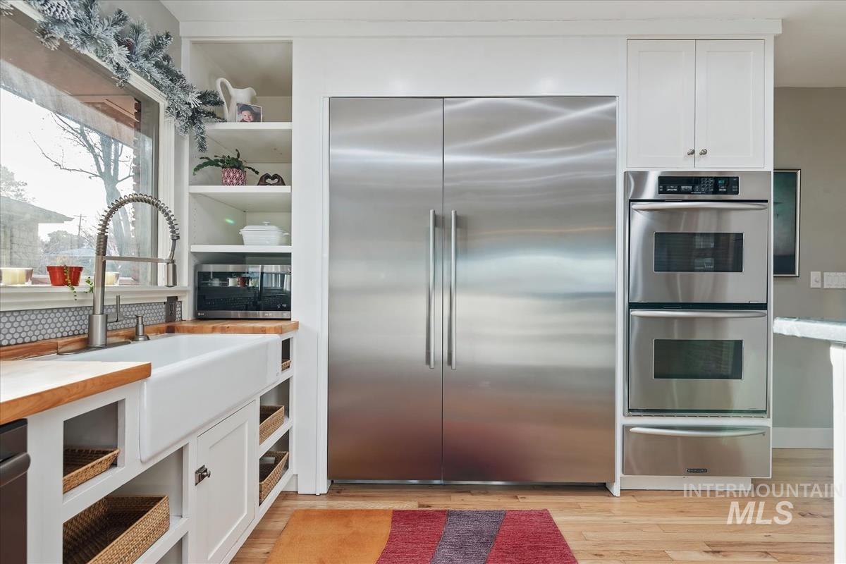 Kitchen with white cabinets, appliances with stainless steel finishes, a warming drawer, and open shelves