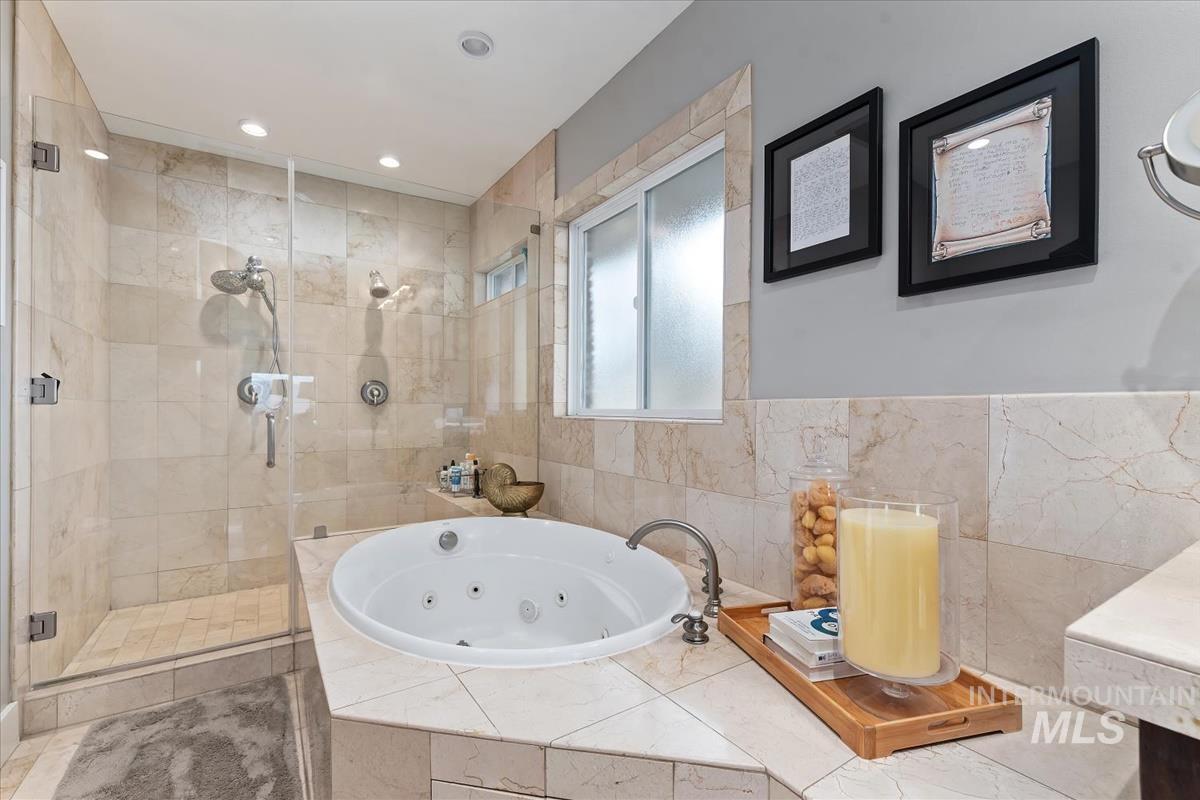 Bathroom featuring a shower stall, a tub with jets, vanity, and recessed lighting