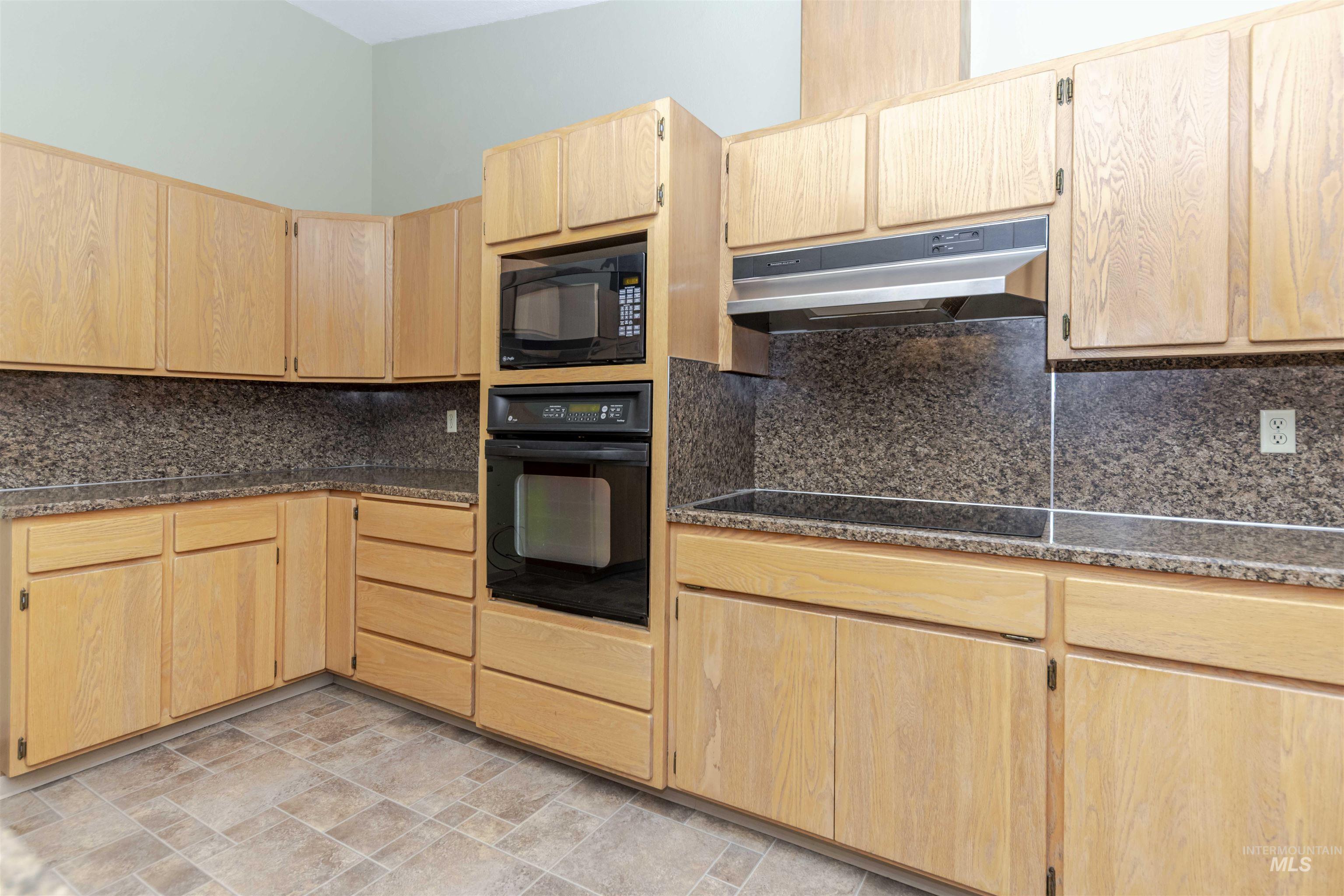 Kitchen featuring light wood finish cabinets, black appliances, backsplash, and stone finish flooring