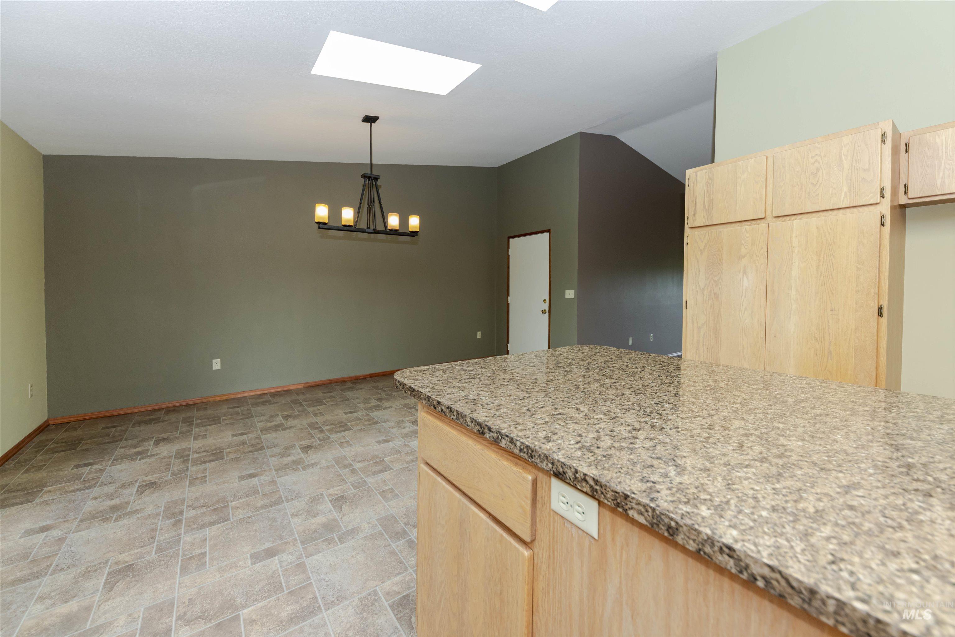 Kitchen with light wood finish cabinets, stone finish flooring, light stone counters, a skylight, and hanging light over dining room