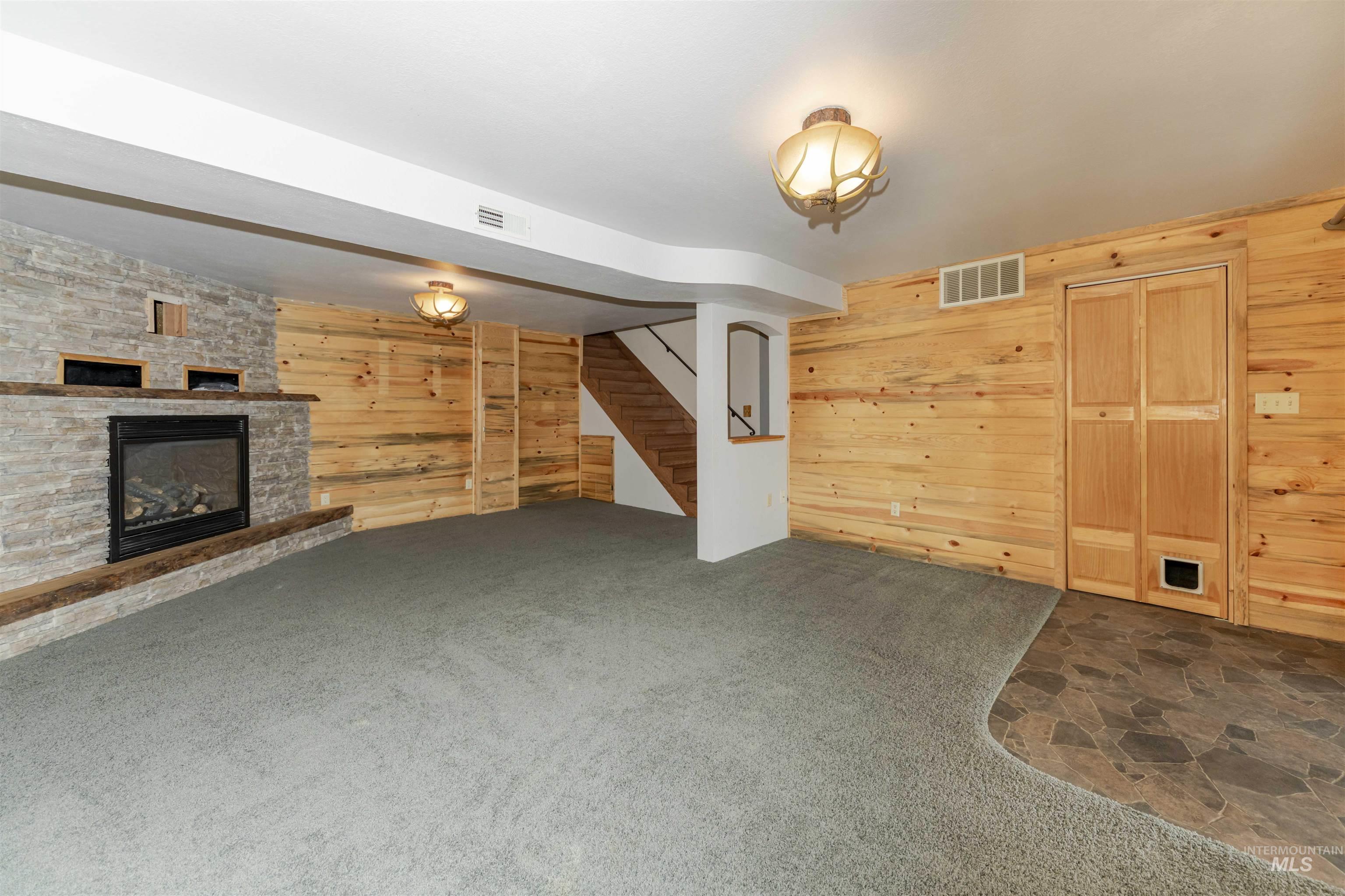Family room featuring wooden walls, a stone fireplace, dark carpet, and dark stone finish floors
