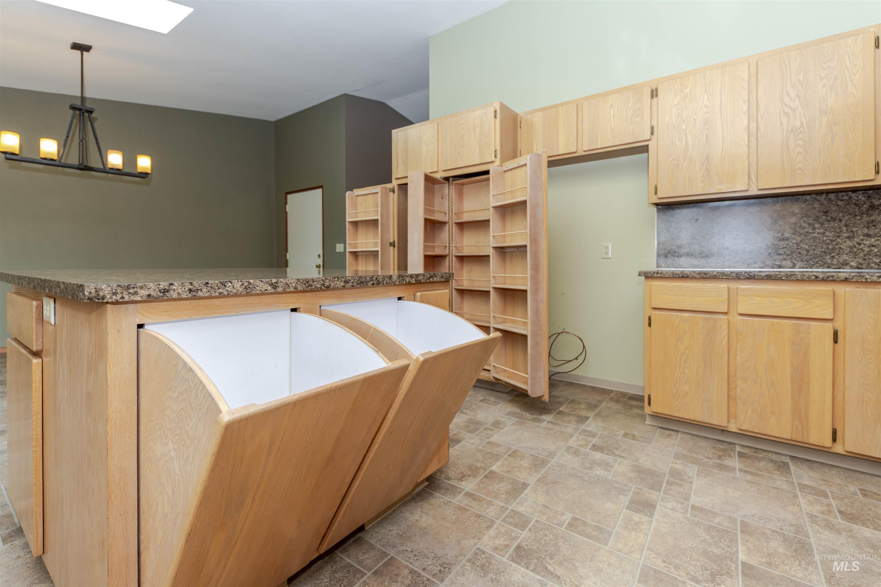 Kitchen with light wood finish cabinetry, stone finish floors, a skylight, hanging lights, and dry food storage