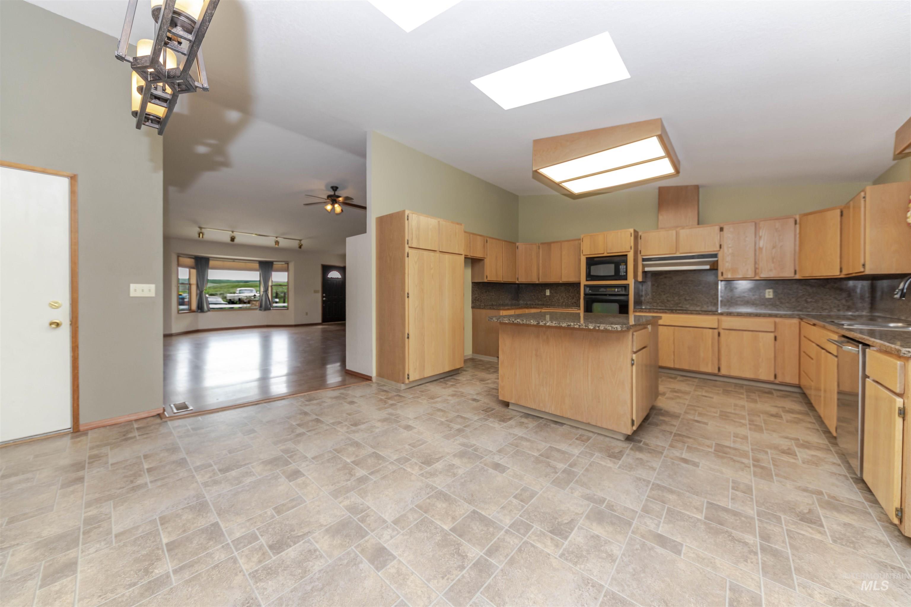 Kitchen with a kitchen island, stone finish floors, light wood finish cabinets, dark stone countertops, and a high ceiling