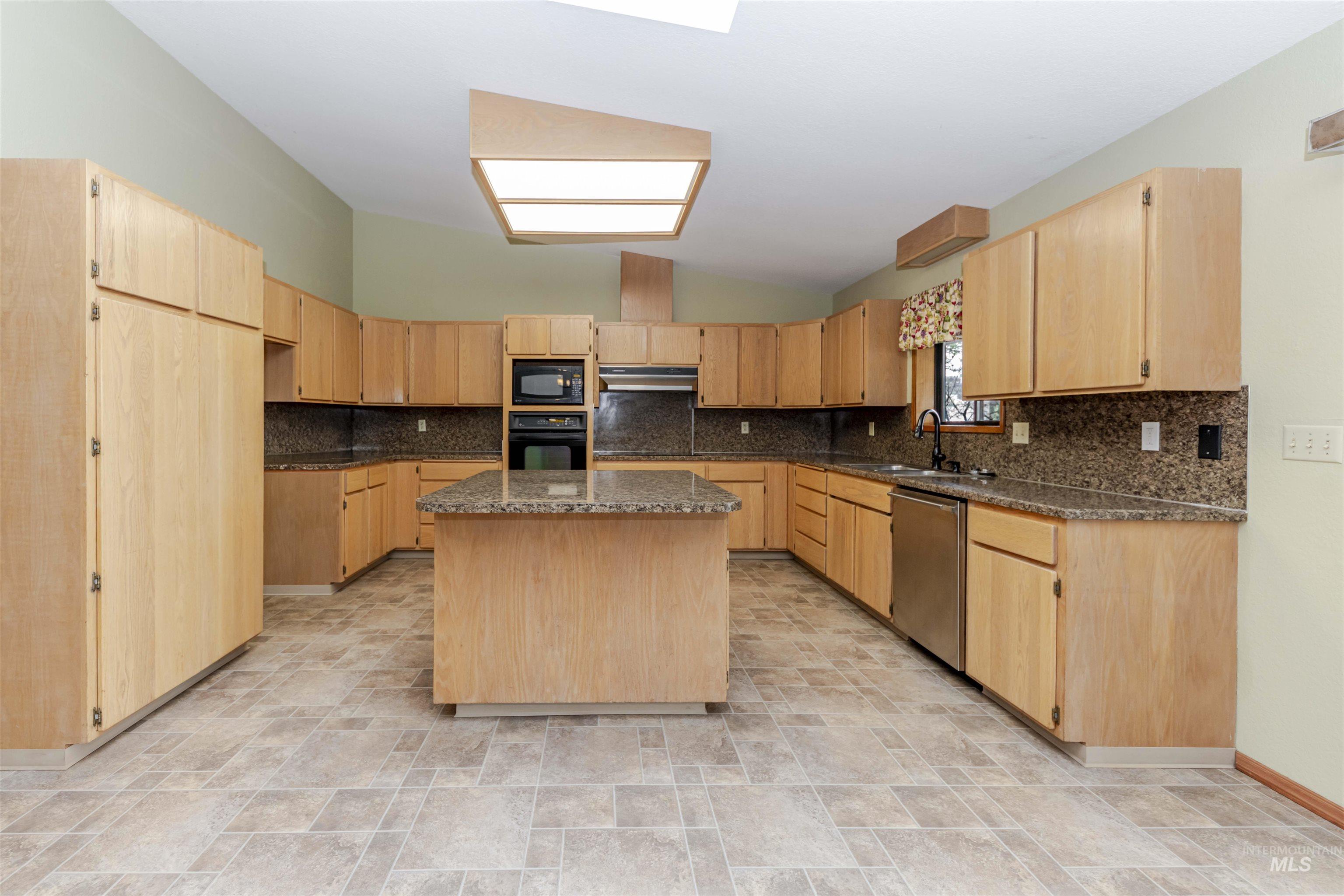 Kitchen featuring light wood finish cabinets, stone finish floors, and lofted ceiling