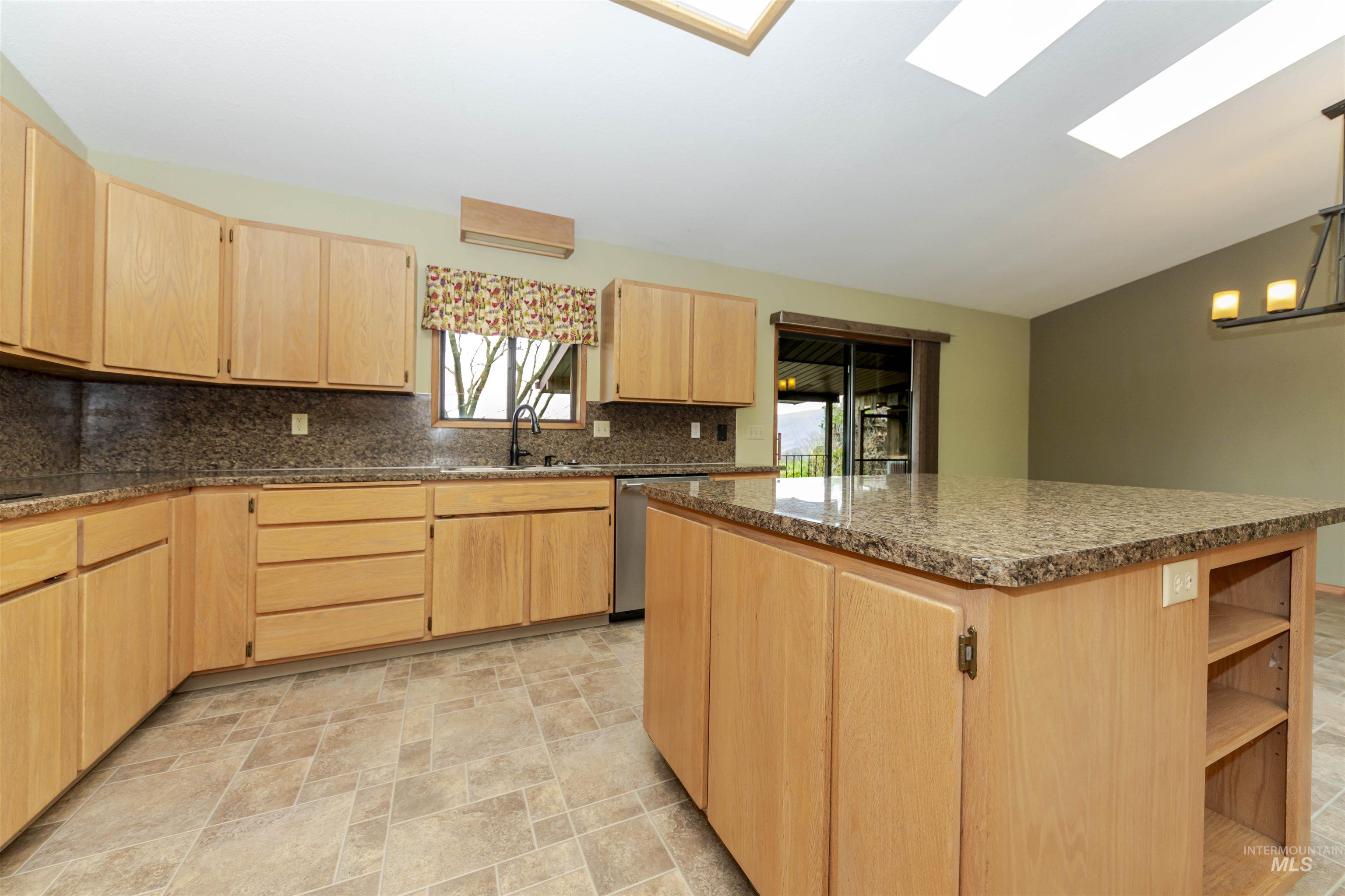 Kitchen featuring light wood finish cabinetry, lofted ceiling, stone finish floors, and open shelves