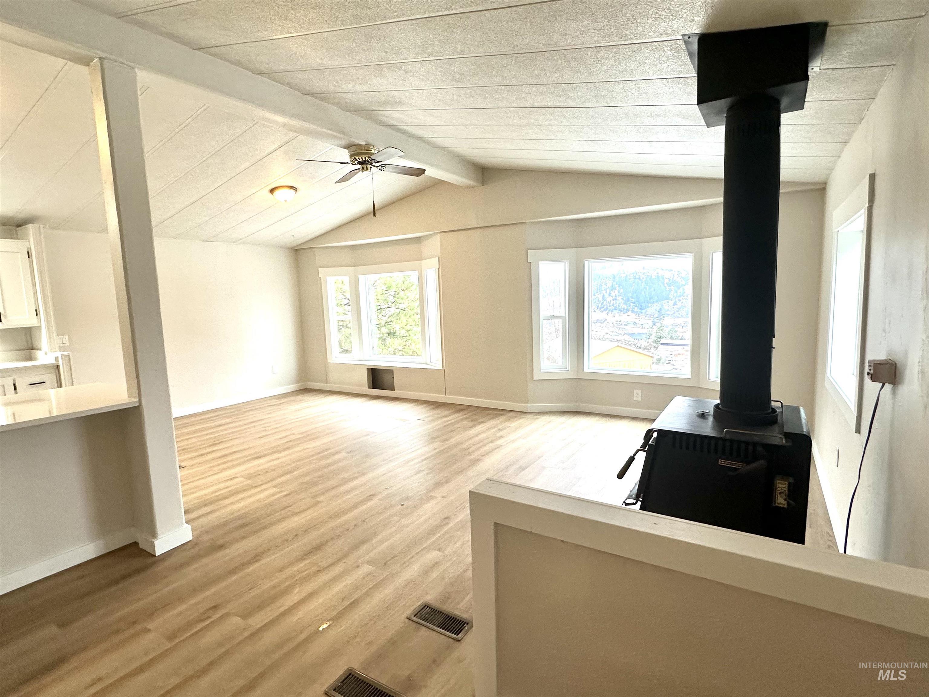 Unfurnished living room featuring a wood stove, light wood-style floors, and ceiling fan