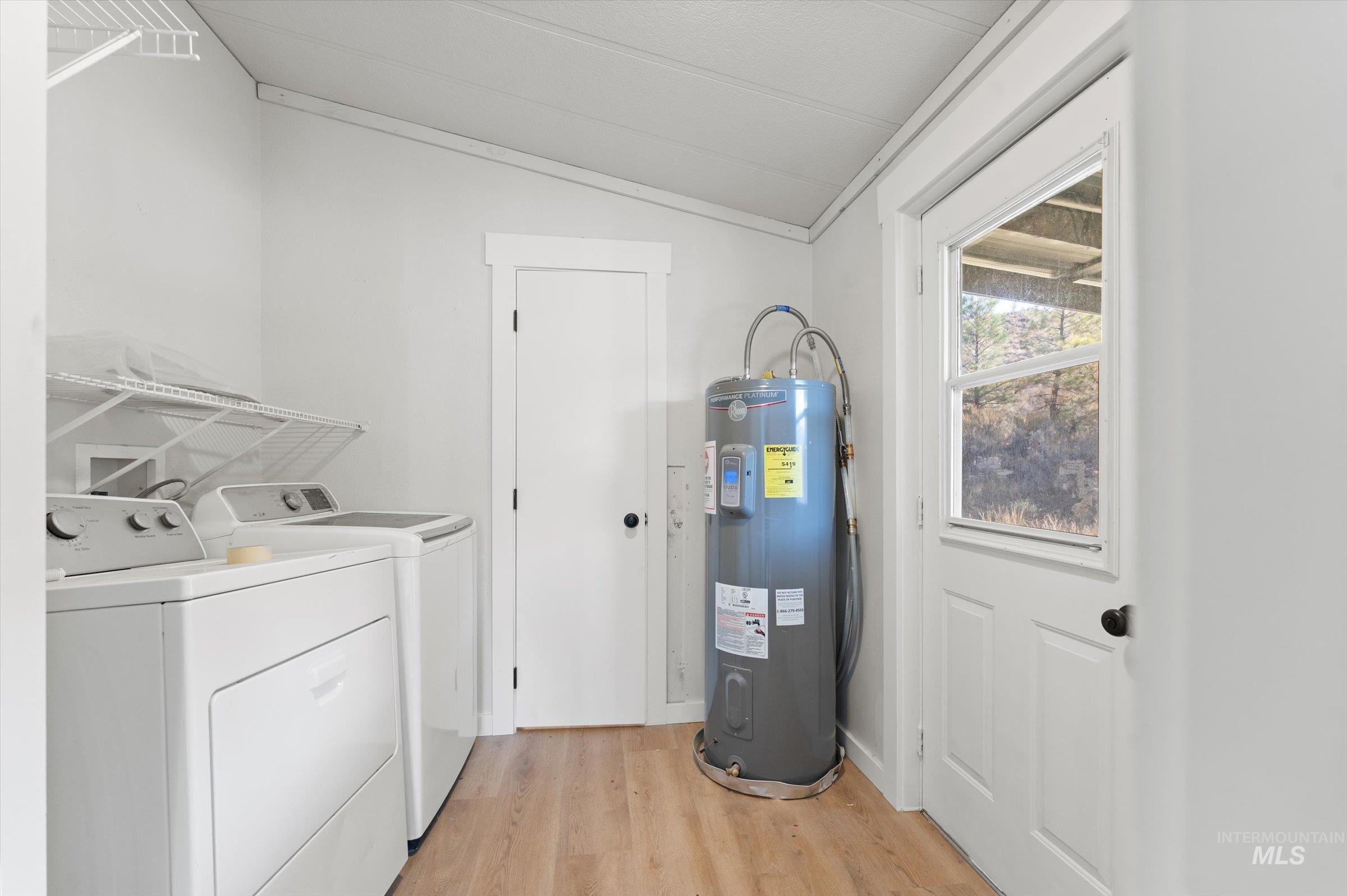 Laundry area with vaulted ceiling, light wood-type flooring, water heater, and washing machine and clothes dryer