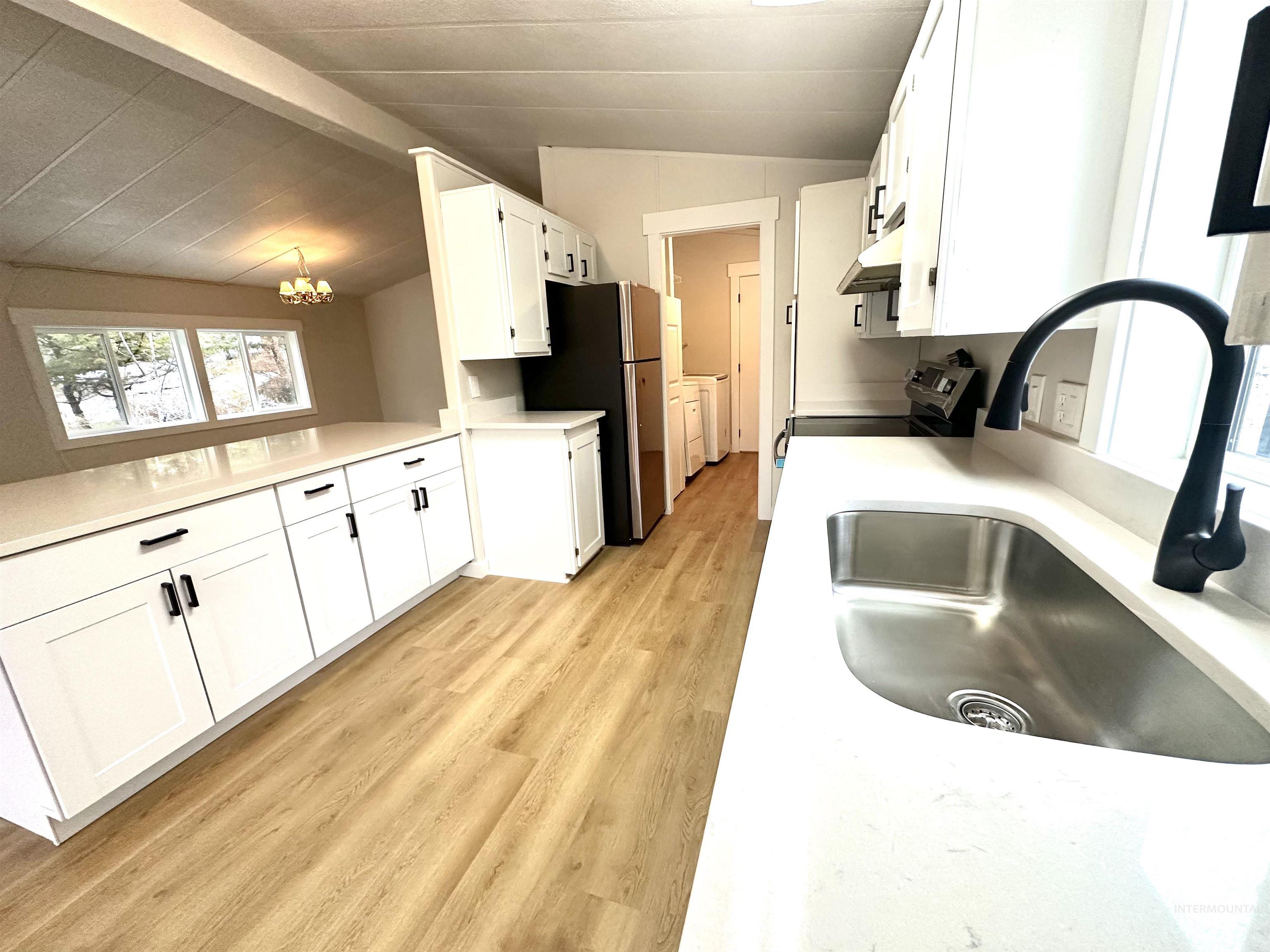Kitchen with white cabinetry, lofted ceiling, light wood finished floors, a chandelier, and under cabinet range hood