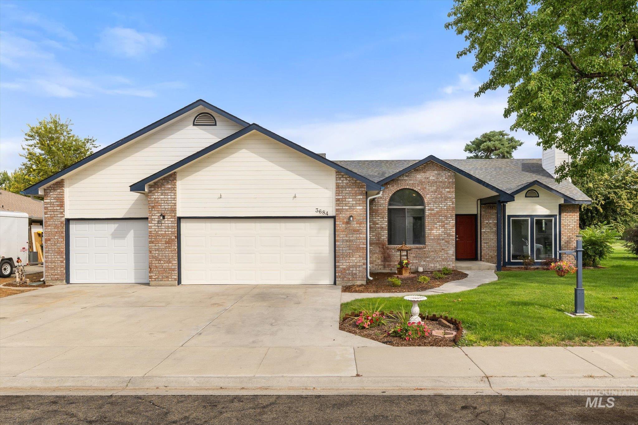 Ranch-style home featuring concrete driveway, an attached garage, a front lawn, brick siding, and a chimney
