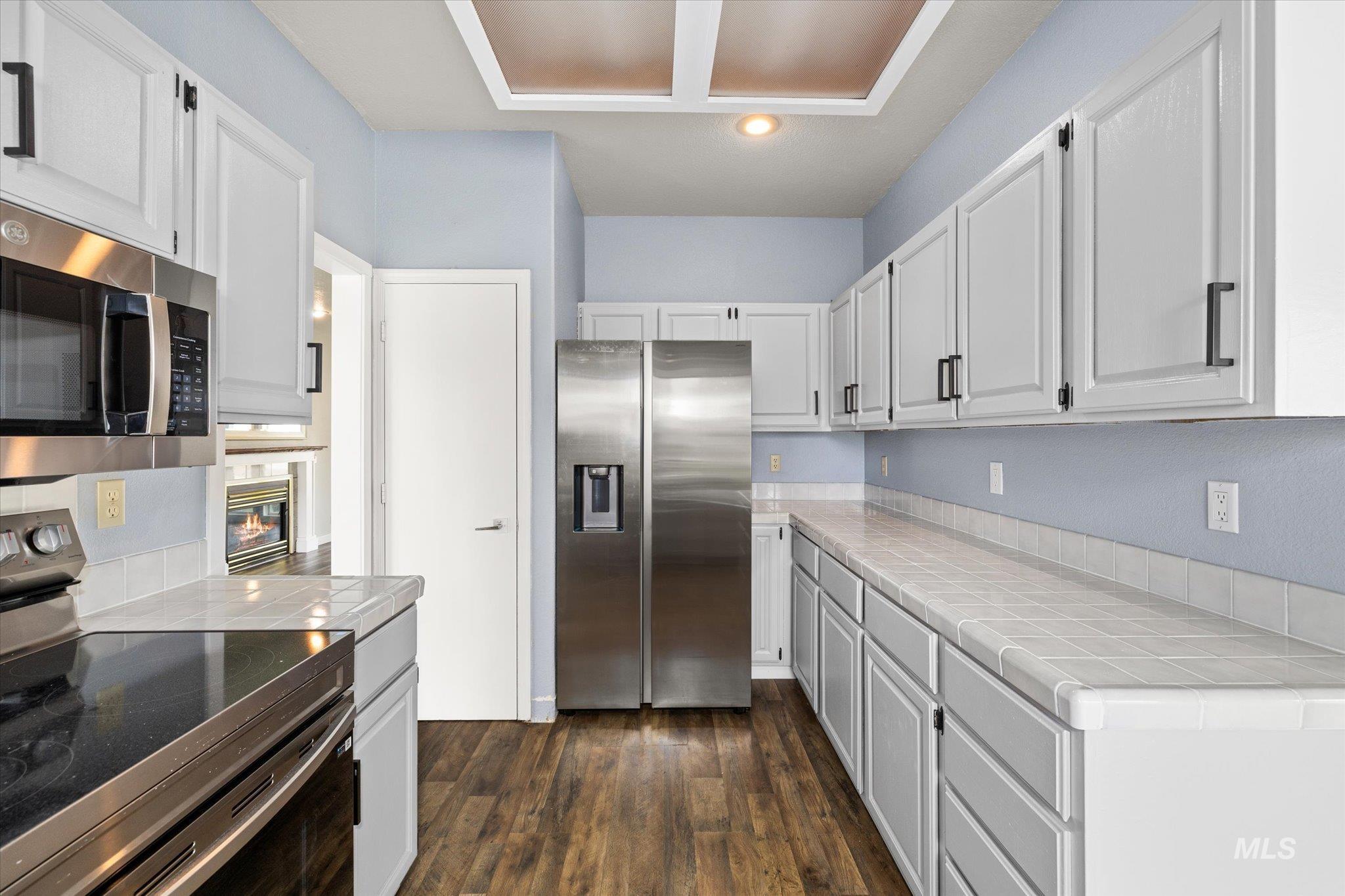Kitchen with appliances with stainless steel finishes, tile counters, dark wood-style floors, and white cabinetry