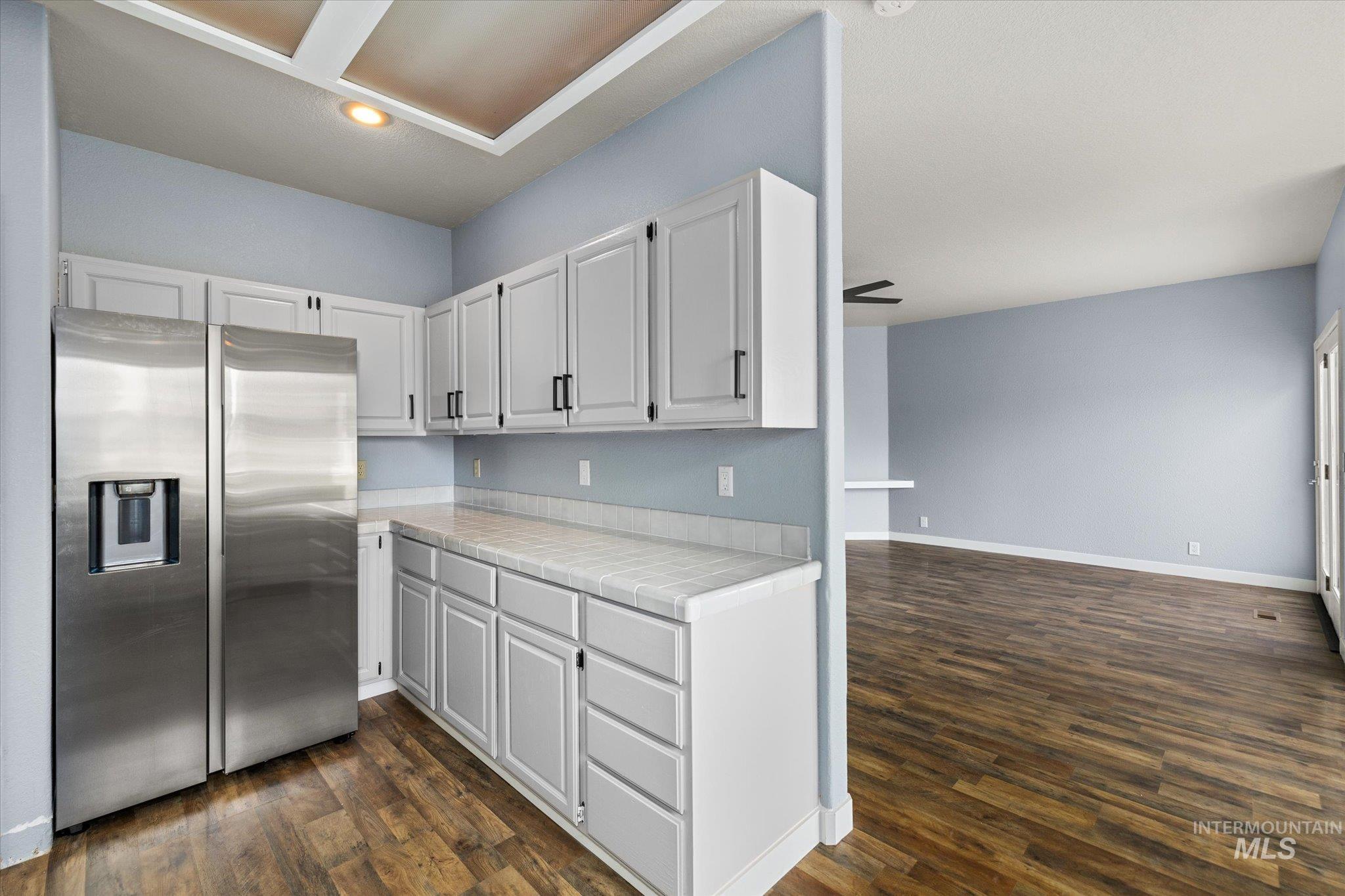 Kitchen with stainless steel refrigerator with ice dispenser, tile counters, dark wood-style floors, white cabinetry, and recessed lighting