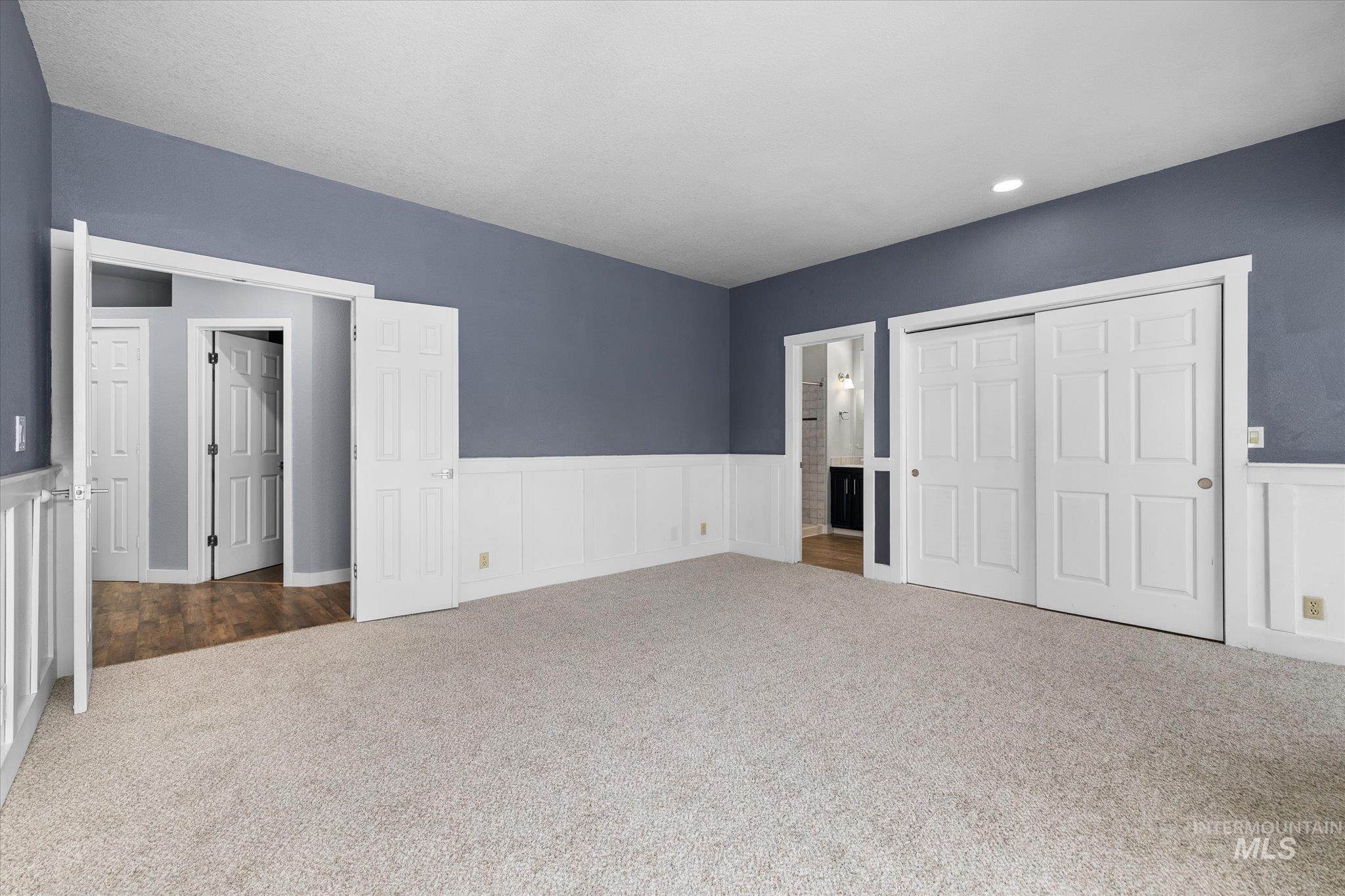 Unfurnished bedroom with carpet floors, a closet, wainscoting, ensuite bath, and a decorative wall