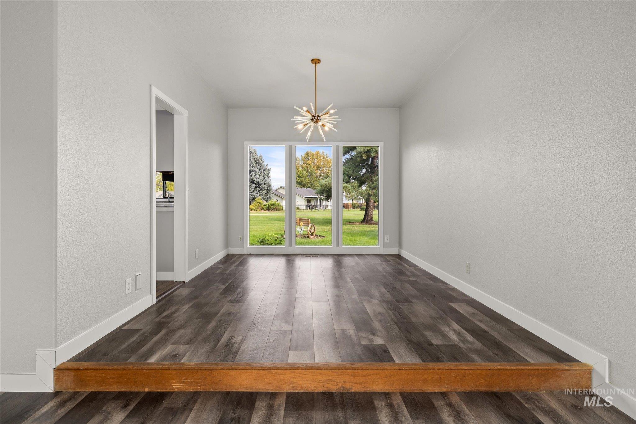 Unfurnished dining area with a chandelier, dark wood-style flooring, and a textured wall