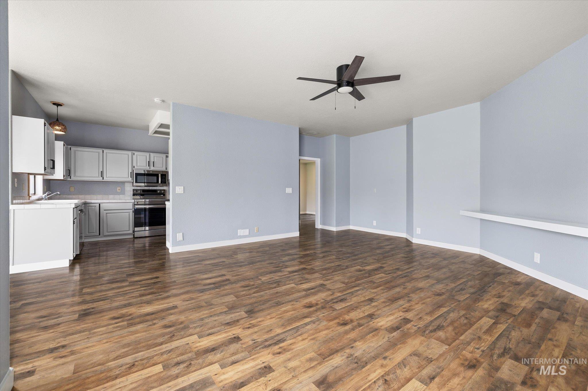 Unfurnished living room featuring dark wood-style flooring and ceiling fan