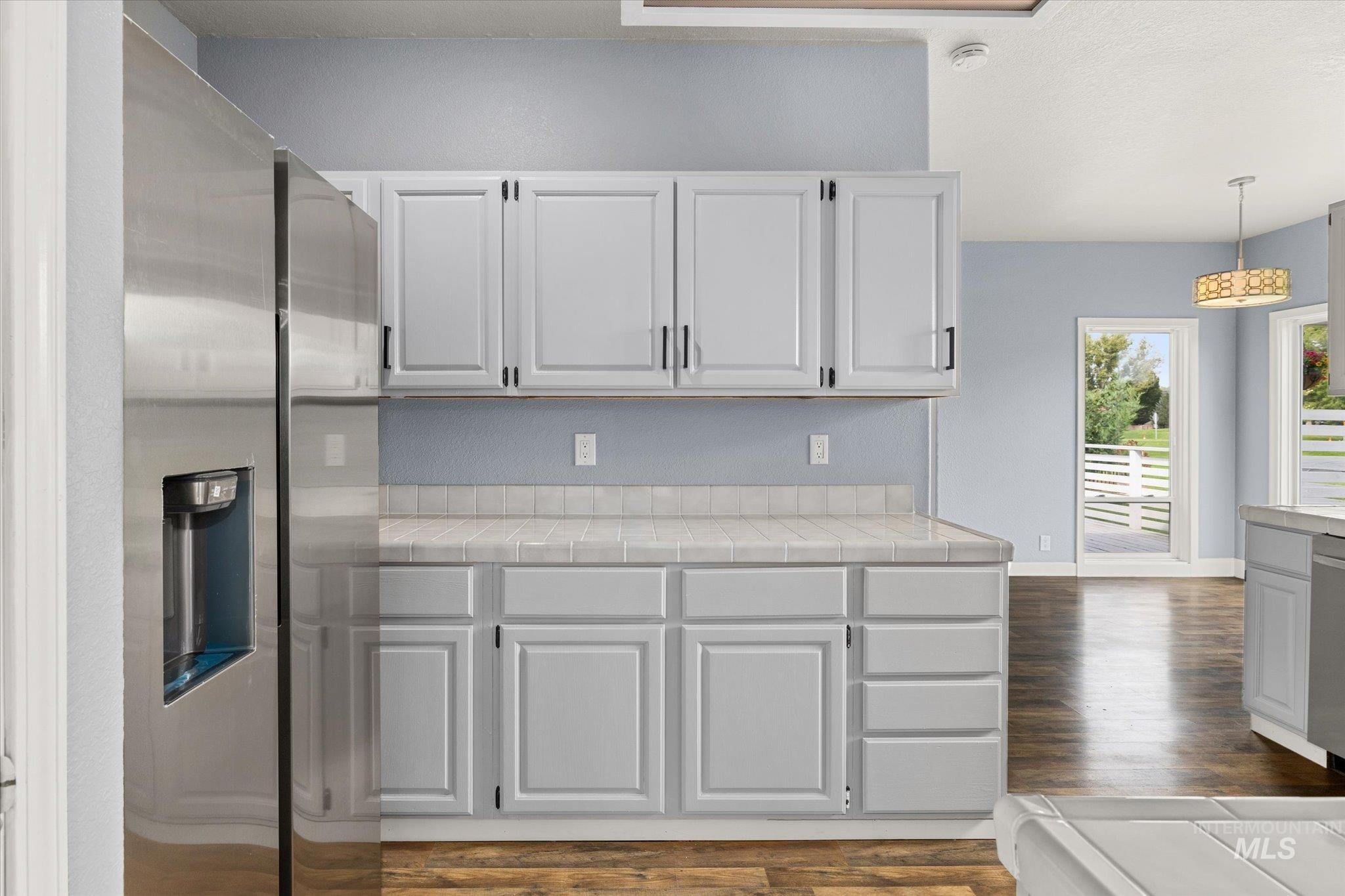 Kitchen with tile countertops, stainless steel appliances, pendant lighting, dark wood-style flooring, and white cabinets