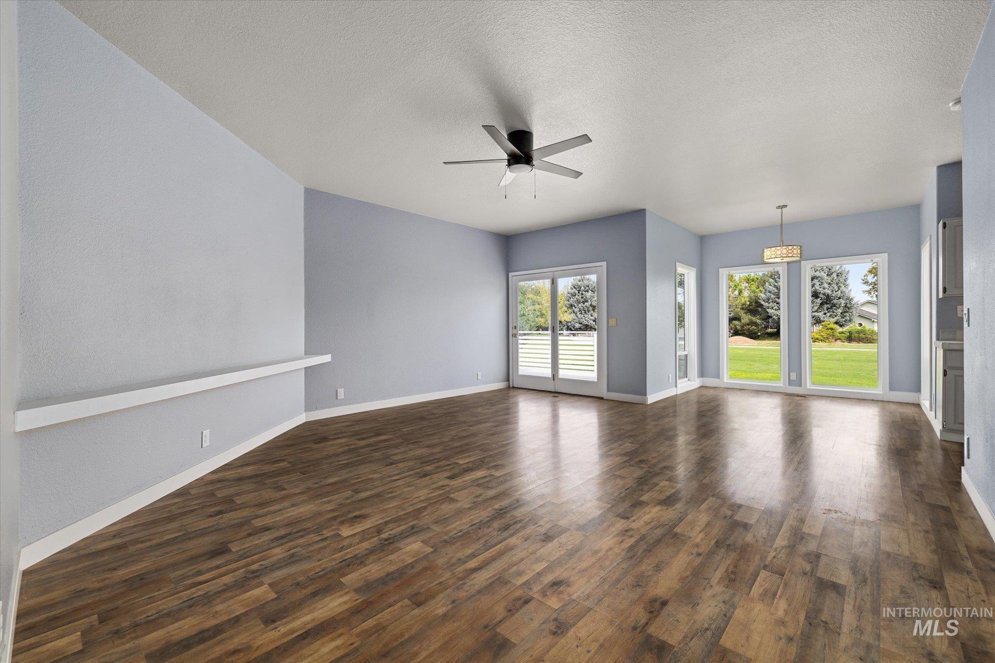 Unfurnished living room with dark wood-style floors, ceiling fan, and a textured ceiling