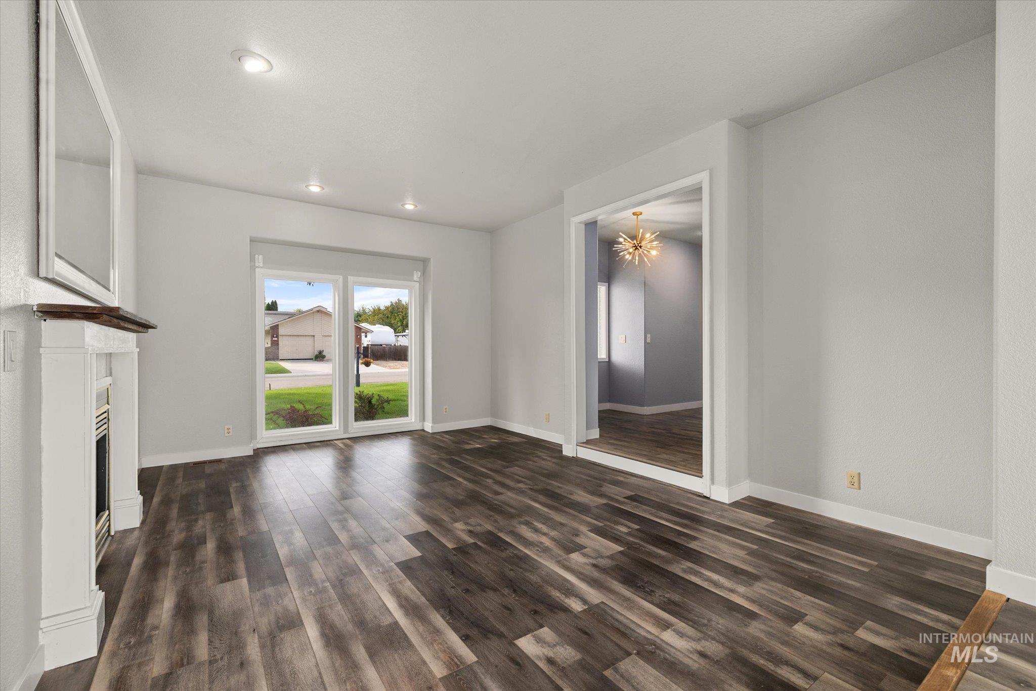 Unfurnished living room featuring dark wood finished floors, a chandelier, a fireplace, and recessed lighting