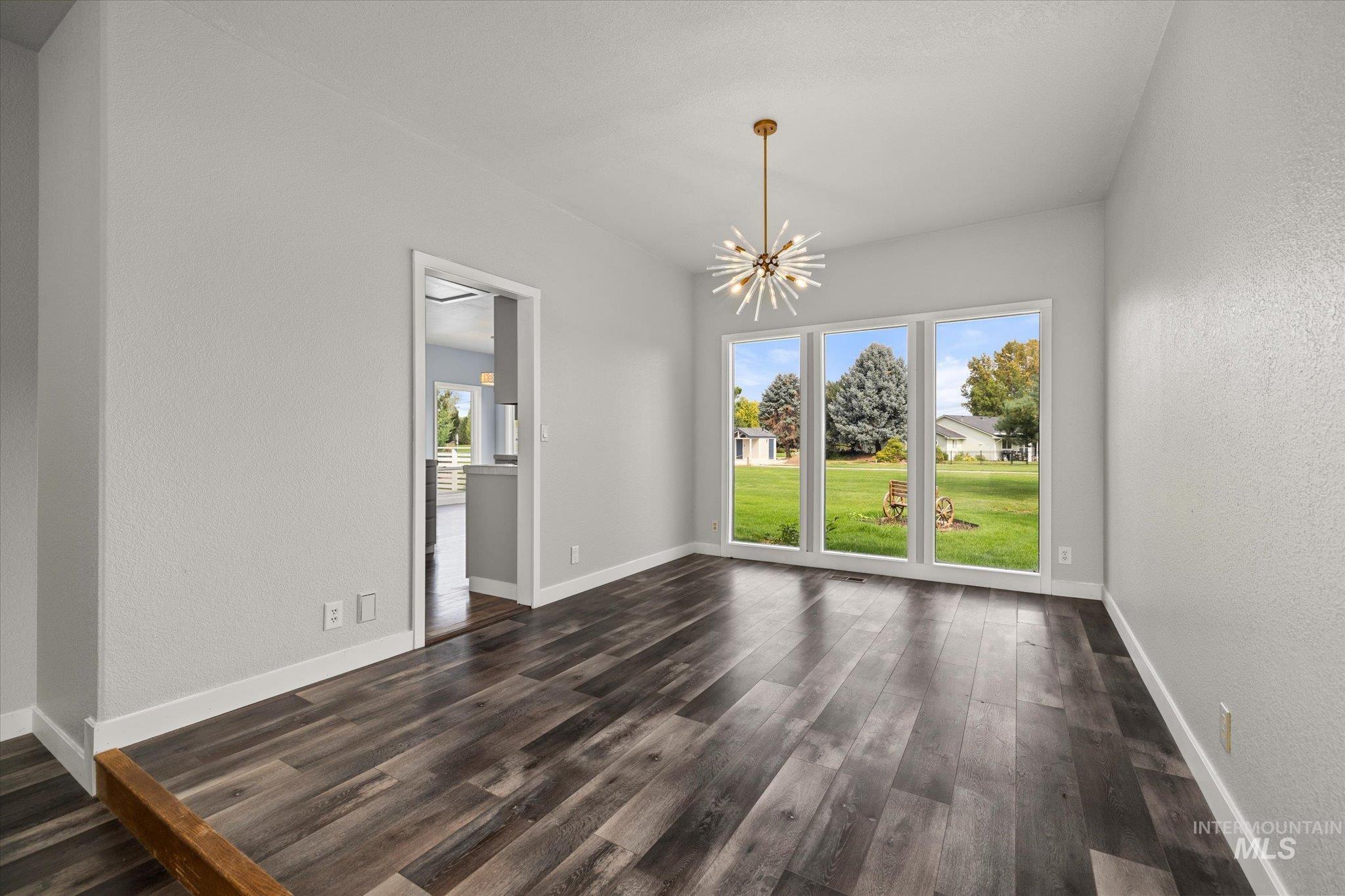 Unfurnished dining area with a textured wall, a chandelier, and dark wood finished floors