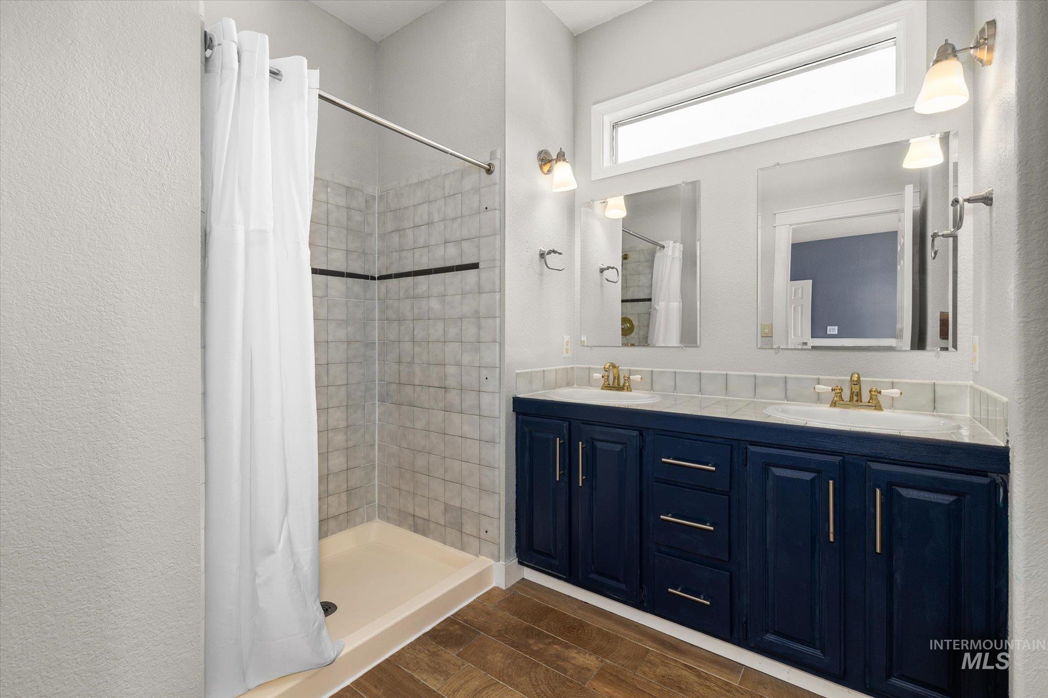 Bathroom with dark wood-type flooring, double vanity, a stall shower, and a textured wall