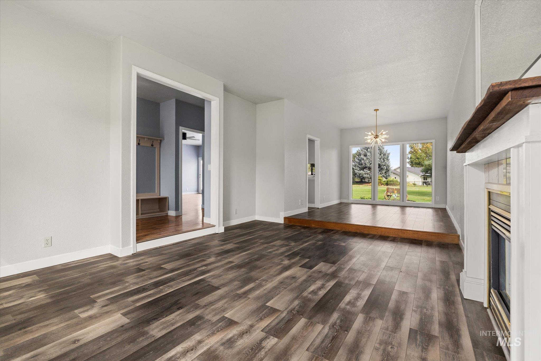 Unfurnished living room with a chandelier, dark wood-type flooring, and a glass covered fireplace