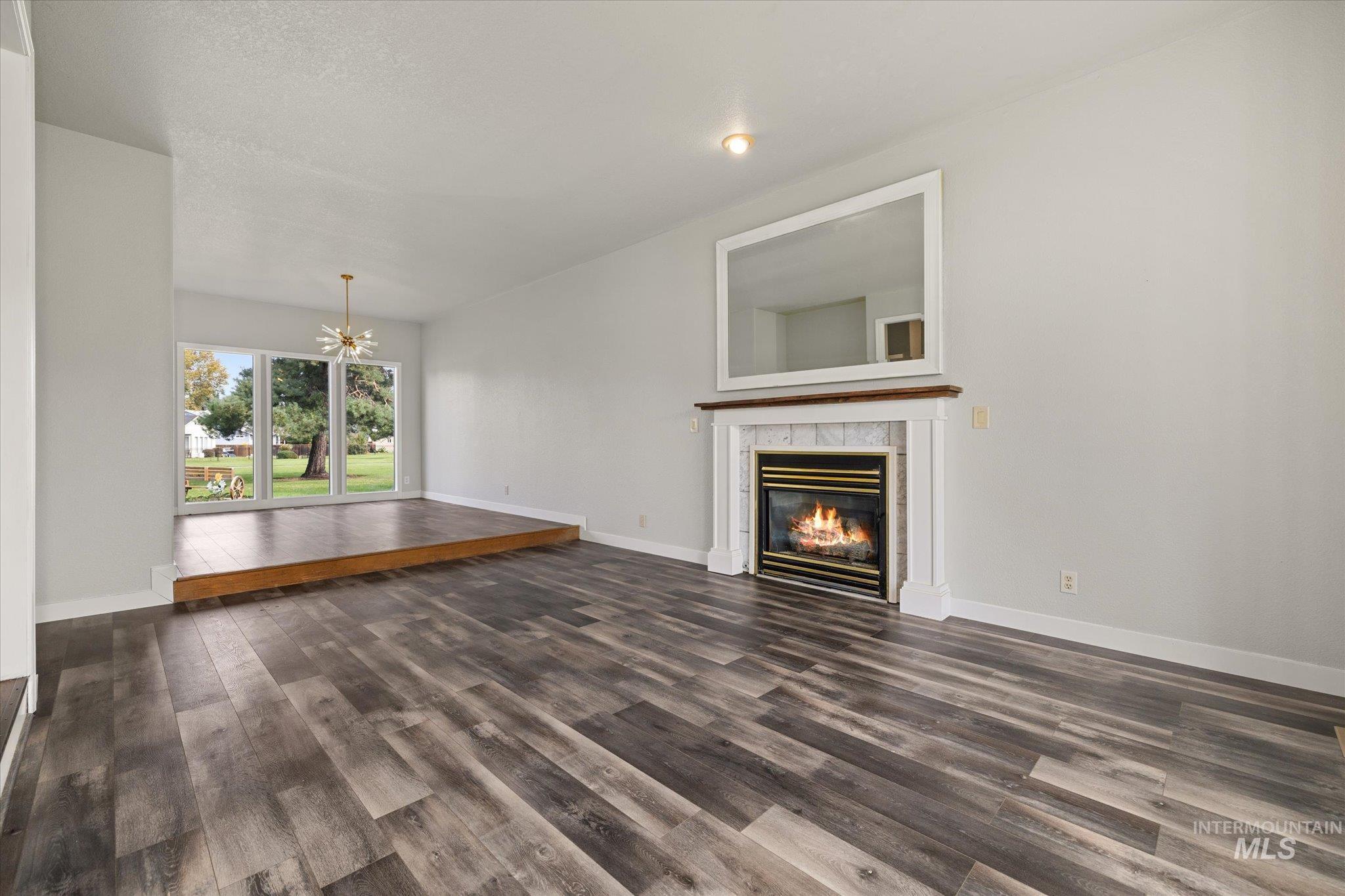 Unfurnished living room featuring a chandelier, dark wood-type flooring, and a tile fireplace