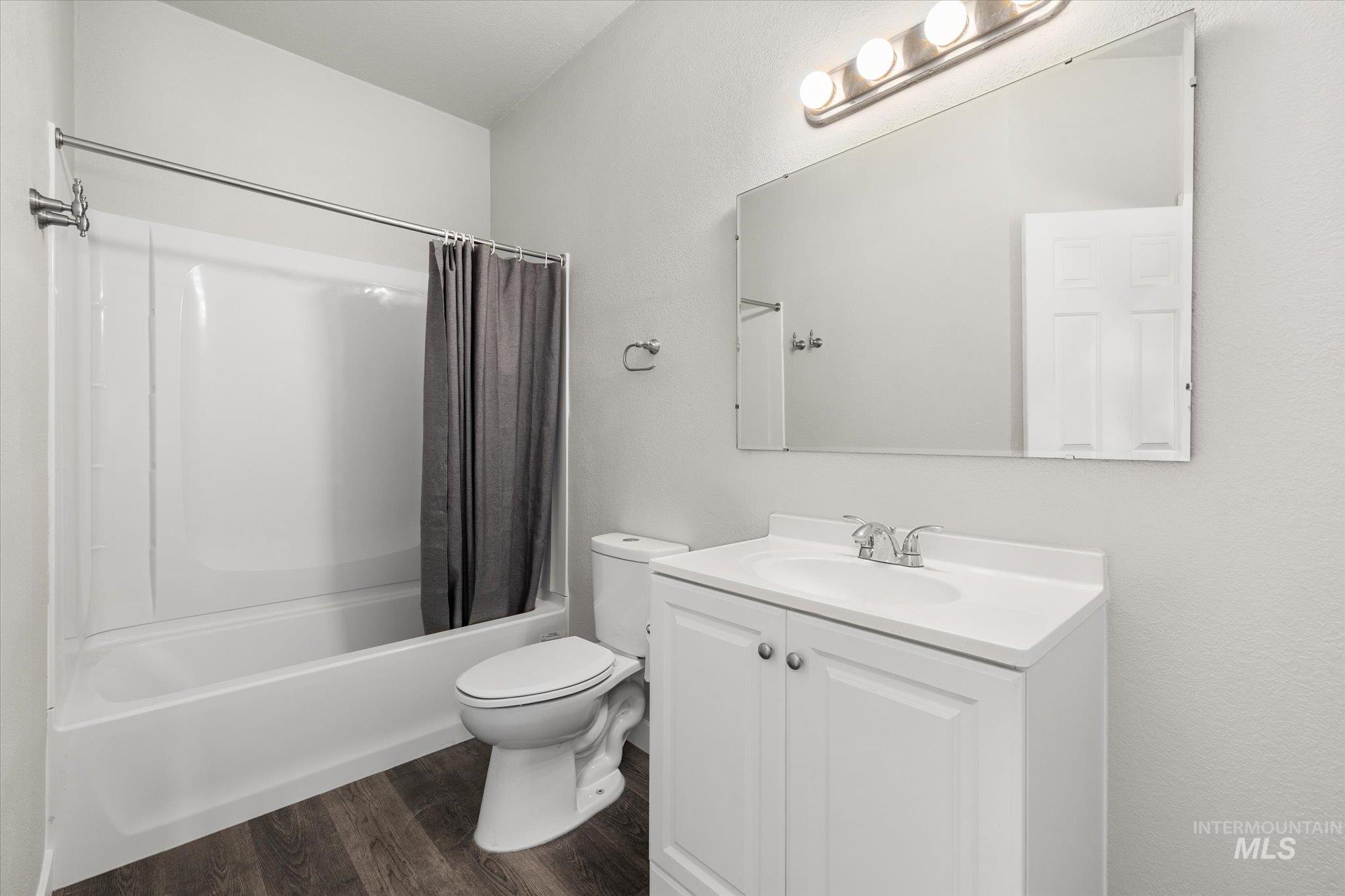 Full bathroom with shower / bath combo with shower curtain, vanity, and dark wood-type flooring