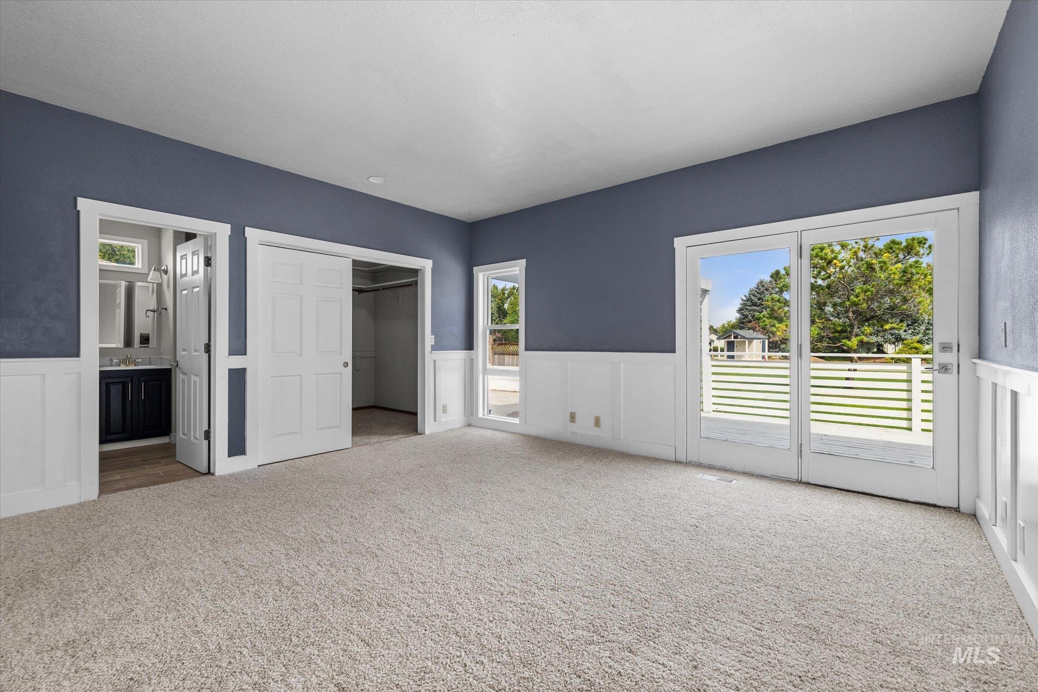 Unfurnished bedroom with a walk in closet, access to exterior, carpet, multiple windows, and a wainscoted wall