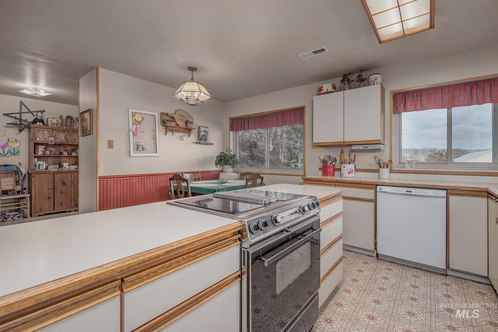 Kitchen with black electric range, light countertops, two tone color scheme, white dishwasher, and decorative light fixtures