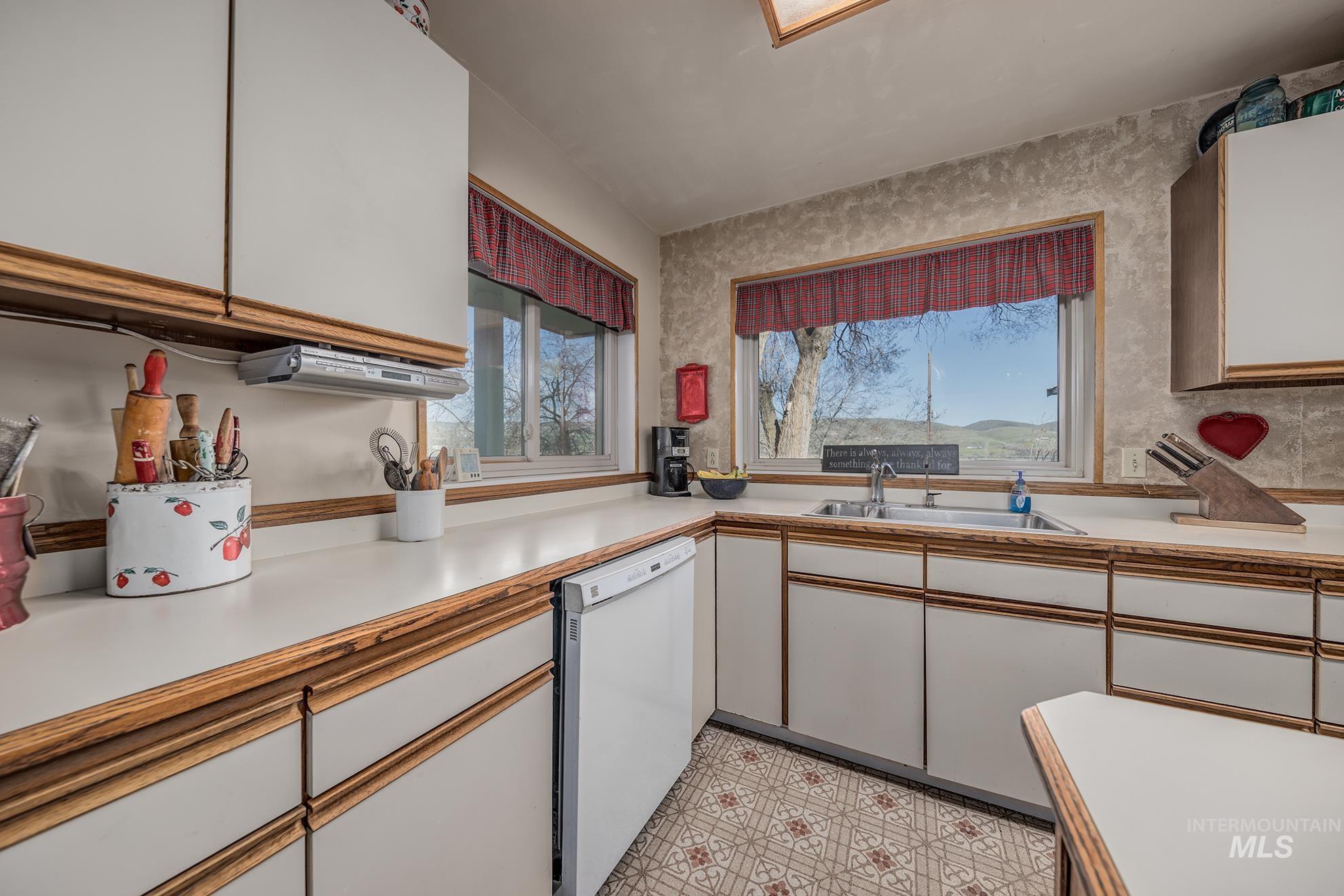Kitchen with two tone cabinetry, light countertops, white dishwasher, and light floors
