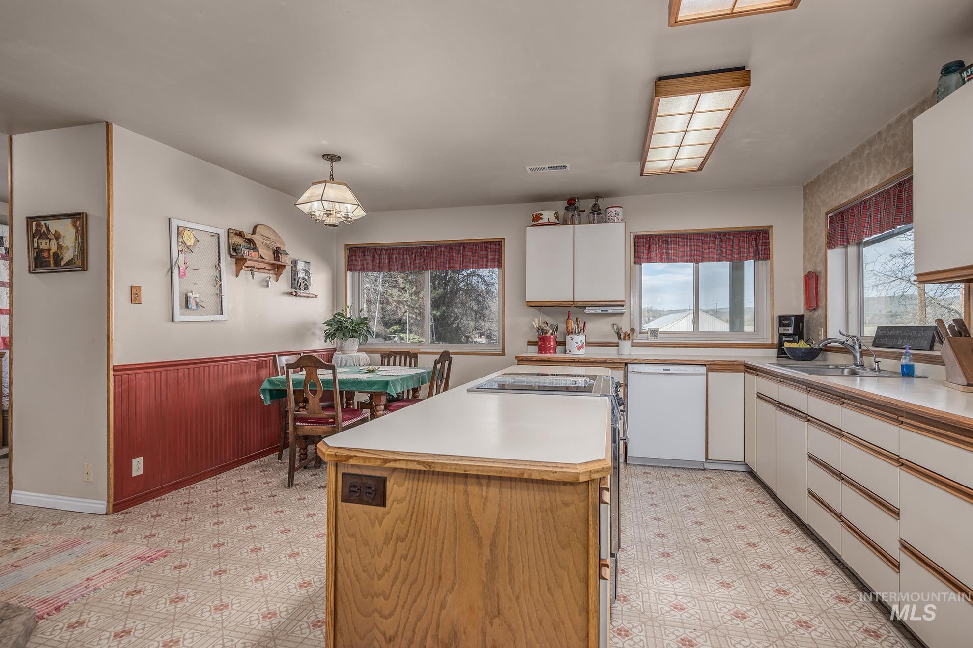 Dual tone kitchen featuring light floors, a wainscoted wall, light countertops, dishwasher, and wood walls