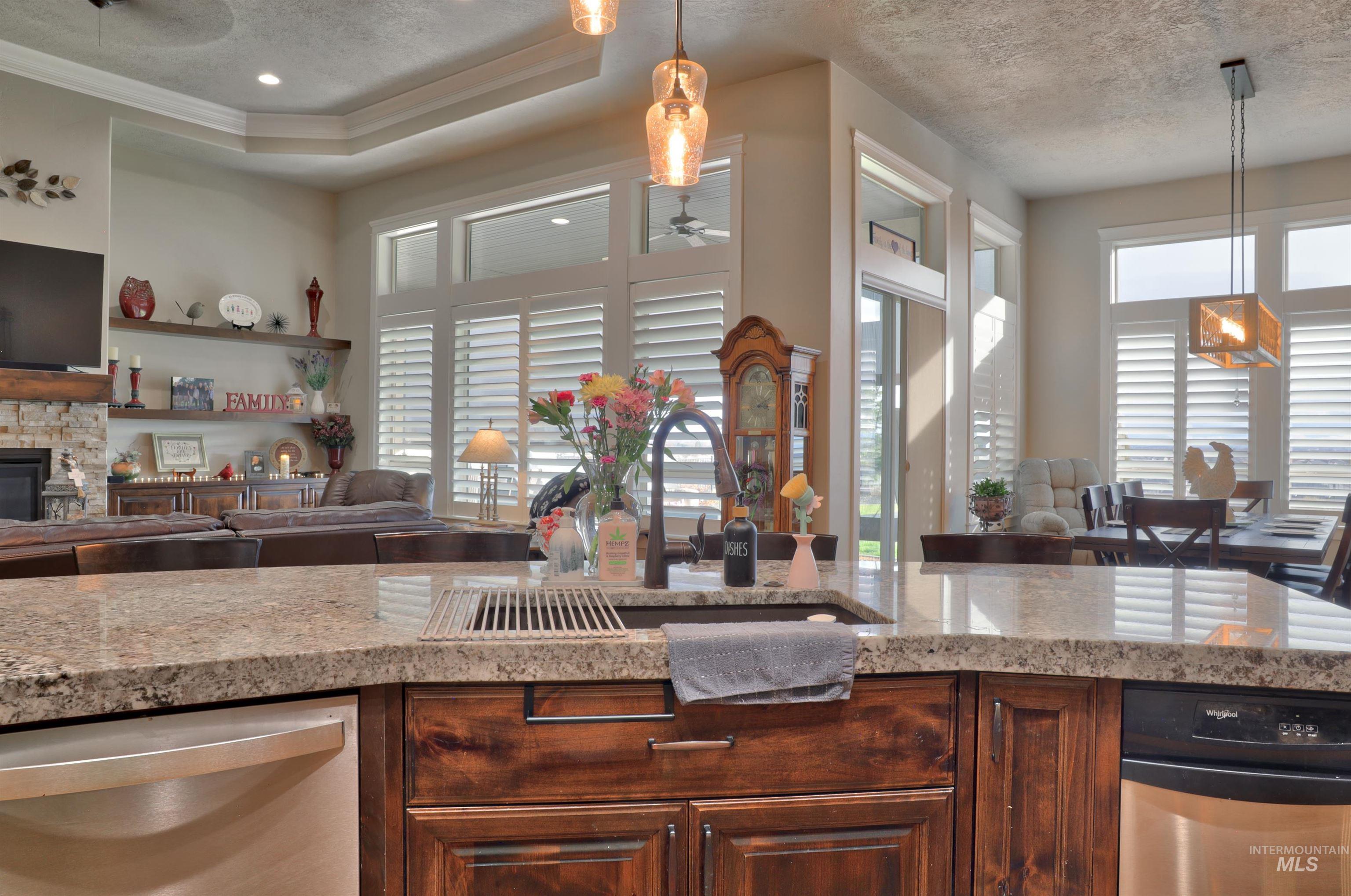 Kitchen featuring open floor plan, stainless steel dishwasher, light stone countertops, hanging light fixtures, and a textured ceiling