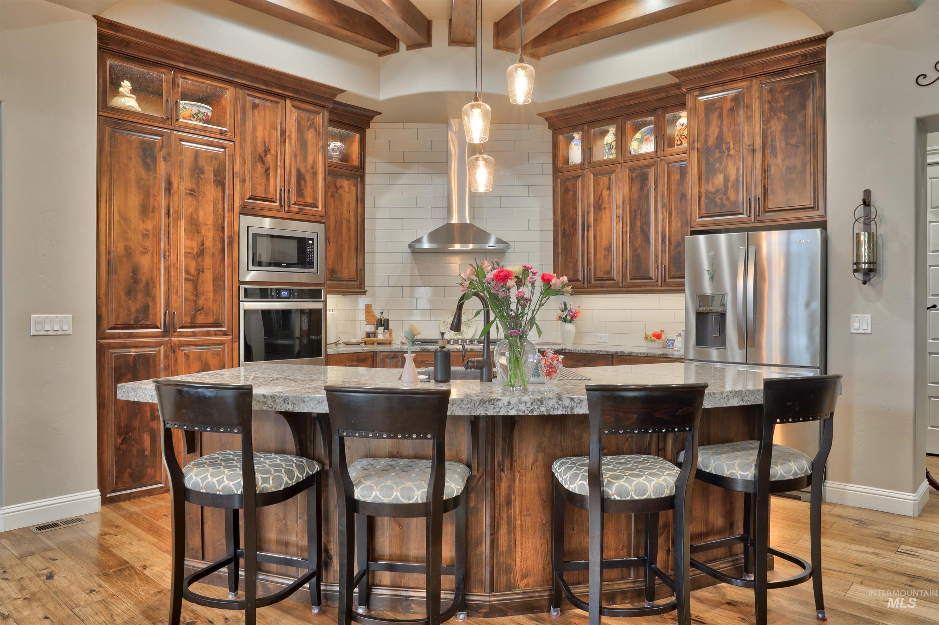 Kitchen featuring hanging light fixtures, appliances with stainless steel finishes, an island with sink, beamed ceiling, and backsplash