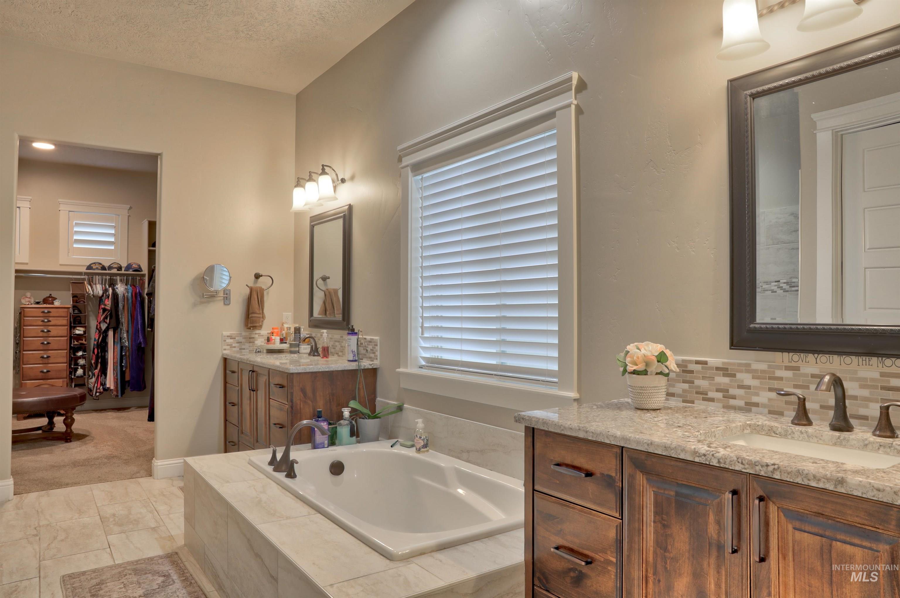 Bathroom with a bath, two vanities, a walk in closet, and a textured ceiling
