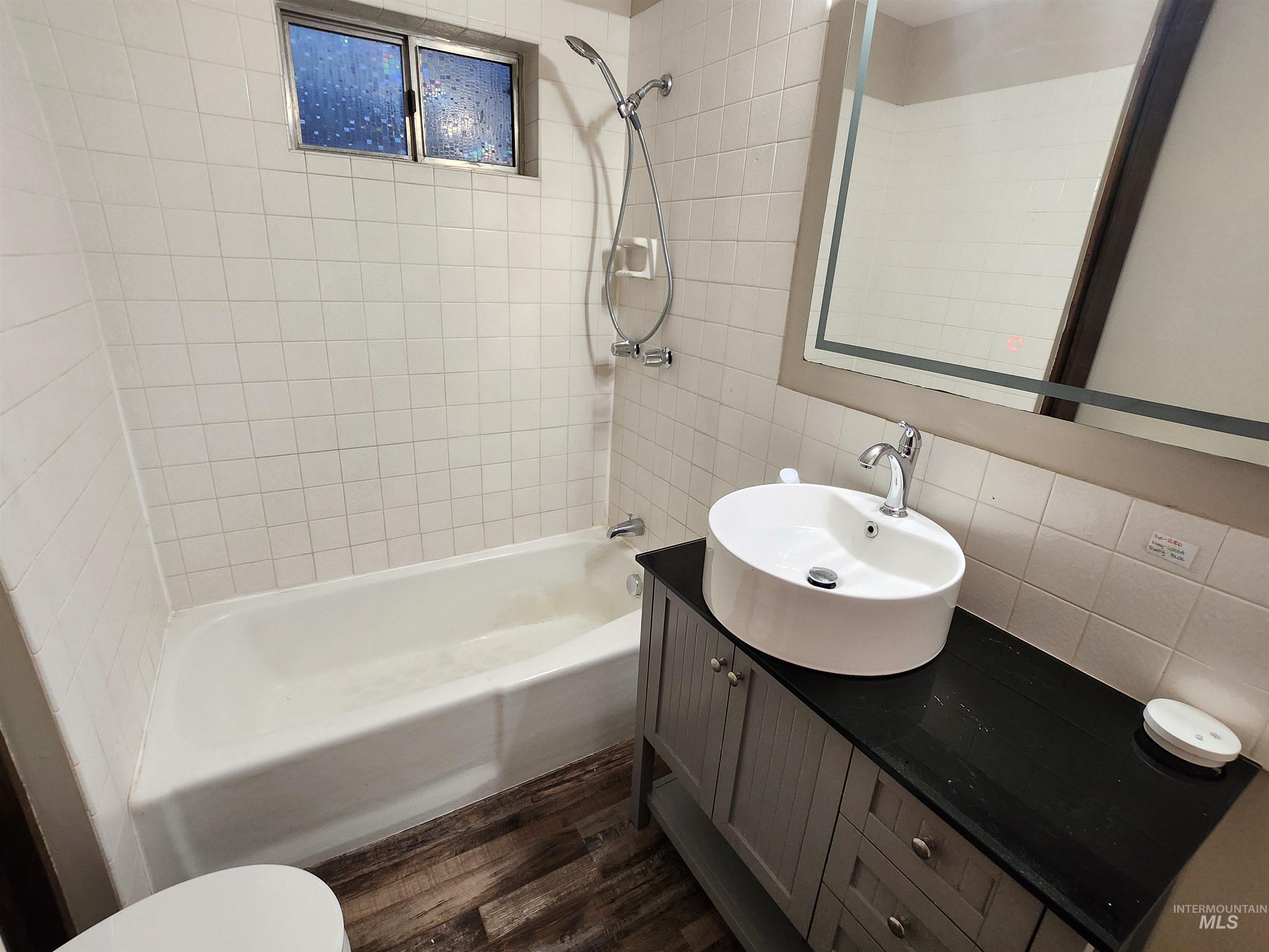 Bathroom with shower / tub combination, vanity, dark wood-style floors, backsplash, and tile walls