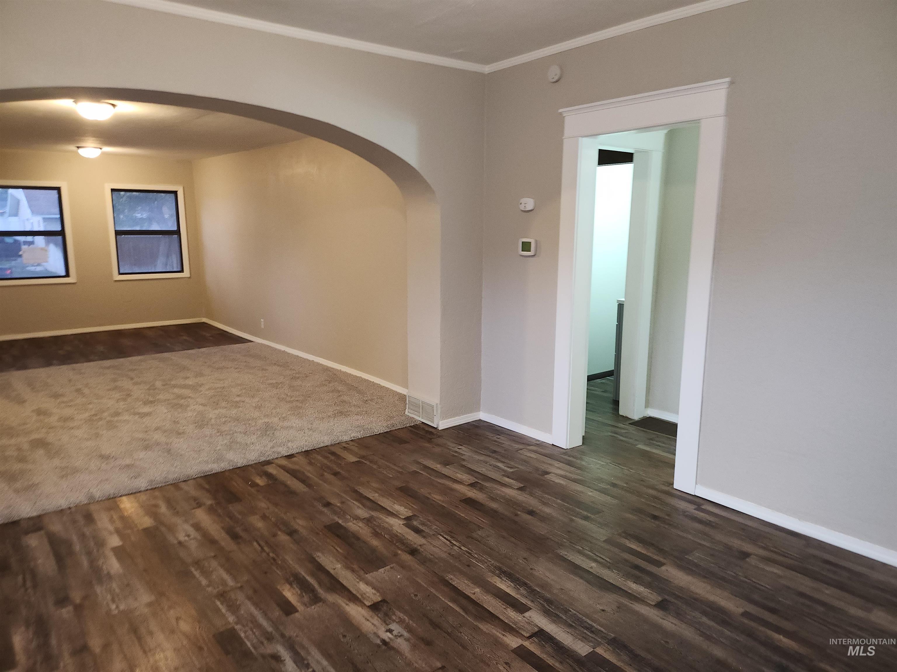 Unfurnished room featuring arched walkways, crown molding, and dark wood finished floors