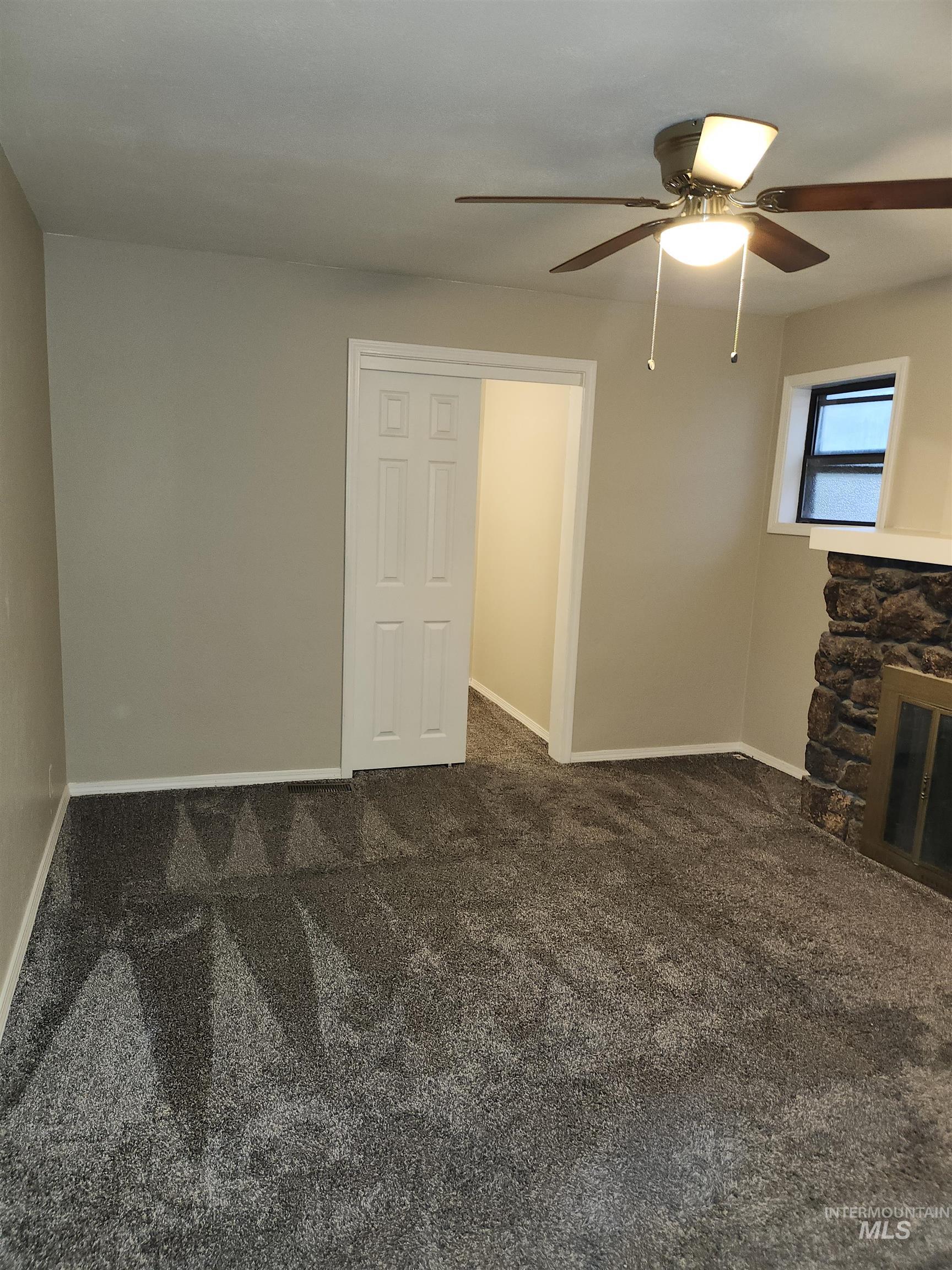 Unfurnished living room featuring dark colored carpet, ceiling fan, and a stone fireplace
