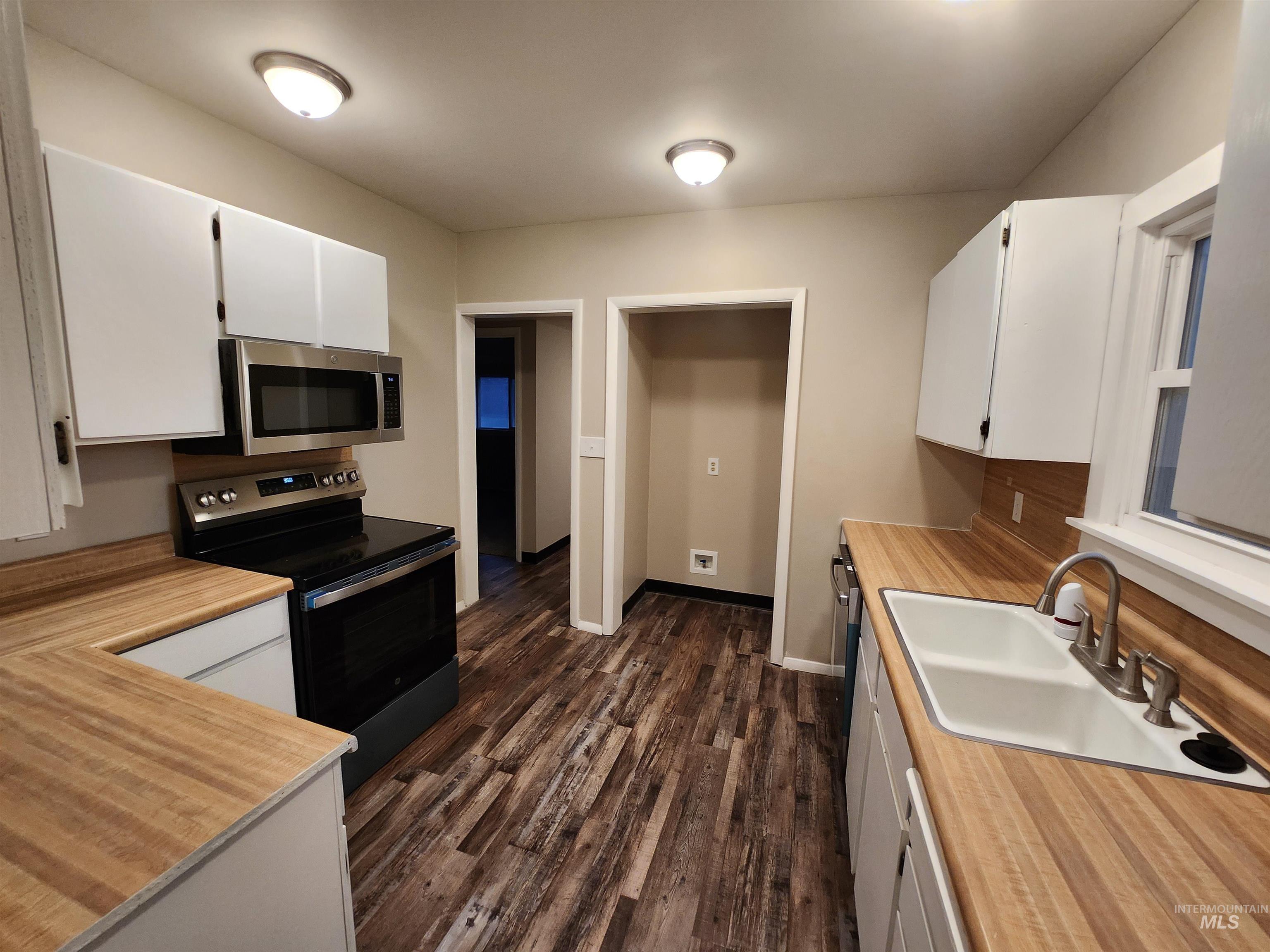 Kitchen featuring electric range, white cabinetry, light countertops, dark wood finished floors, and white dishwasher