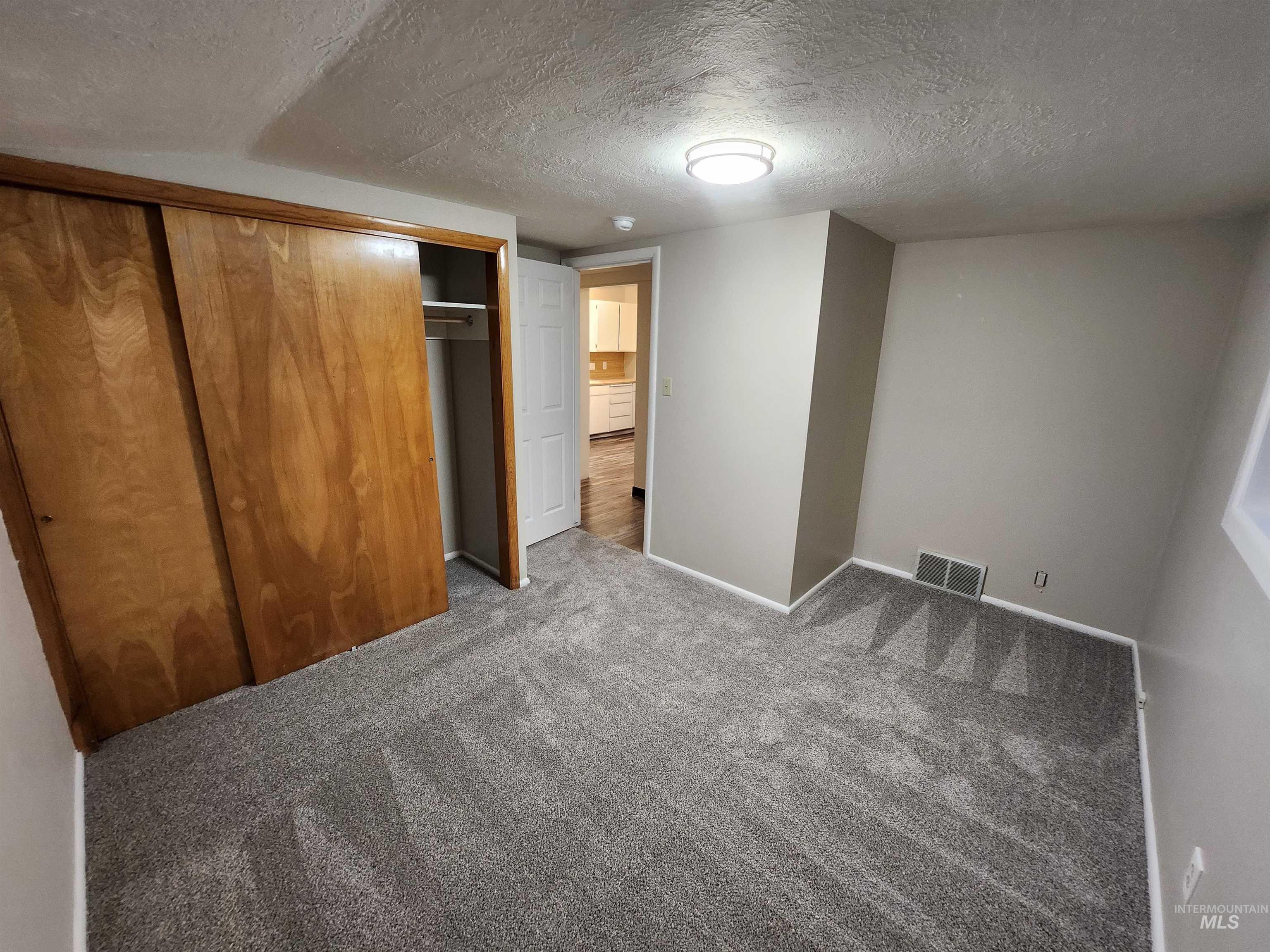 Unfurnished bedroom featuring a textured ceiling, a closet, and dark colored carpet