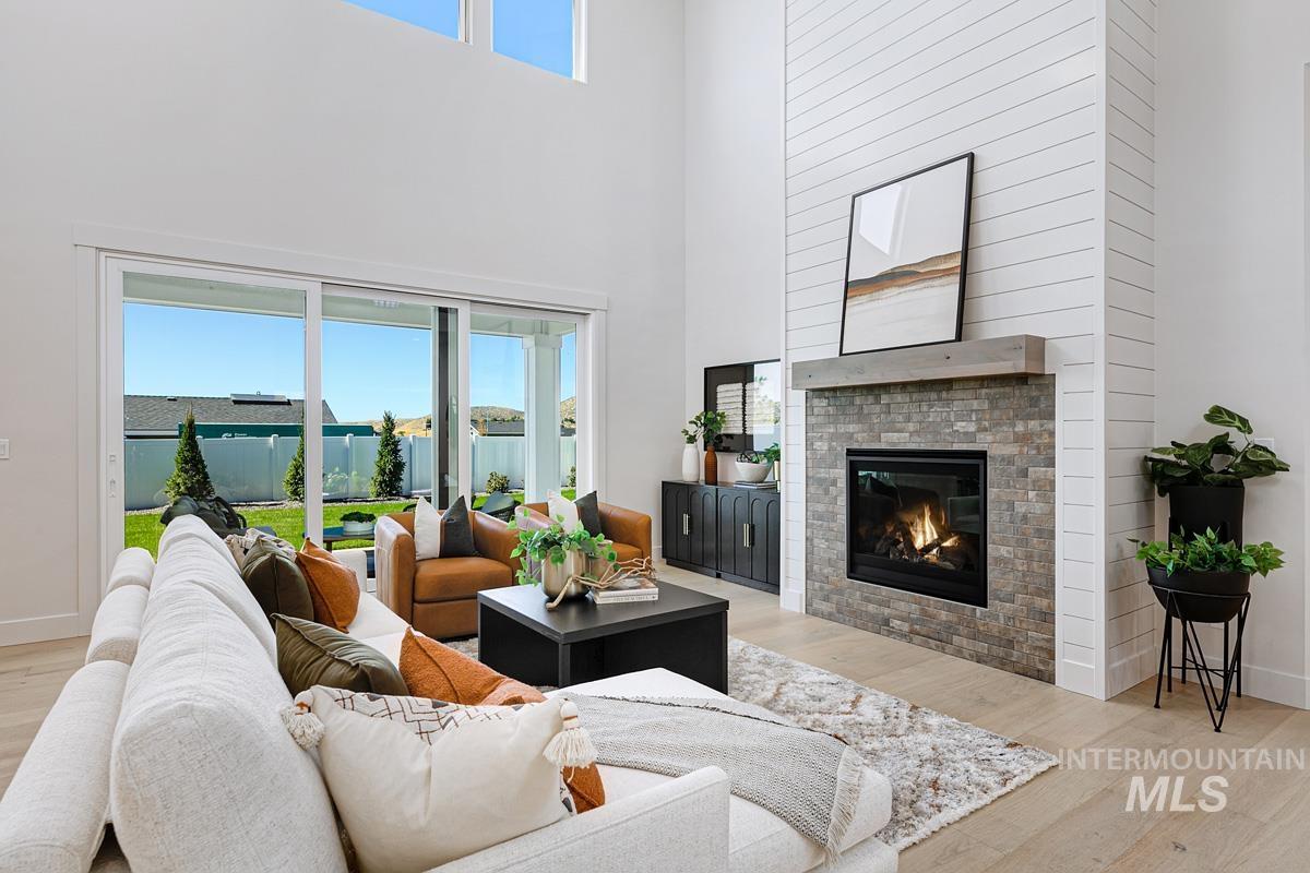 Living room featuring light wood-style flooring, a towering ceiling, and a glass covered fireplace