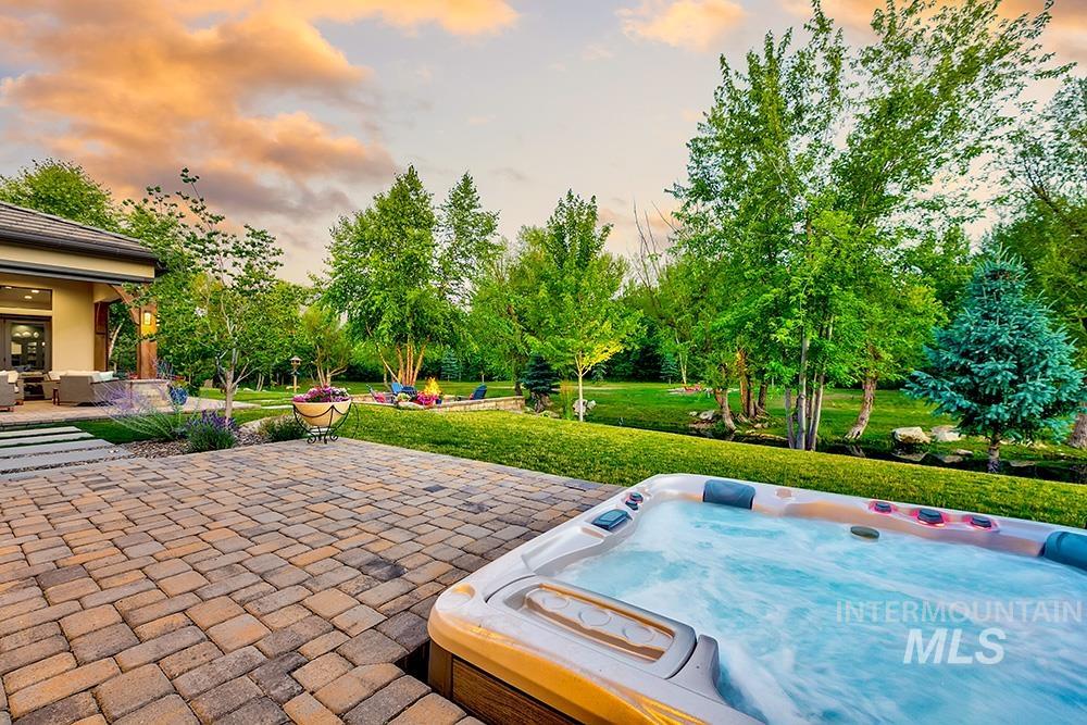 Patio terrace at dusk with a yard, a hot tub, a patio, and view of wooded area