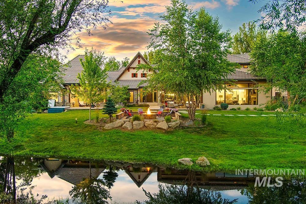 Back of house at dusk featuring a patio, a fire pit, a lawn, stucco siding, and a water view