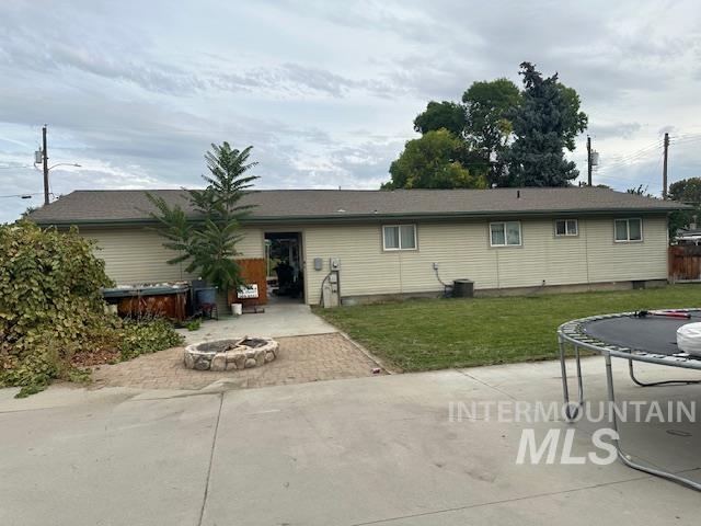 Rear view of house with a trampoline, a patio, an outdoor fire pit, and a yard