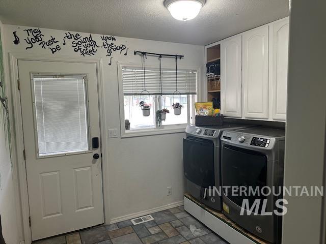 Washroom with stone finish floors, a textured ceiling, separate washer and dryer, and cabinet space