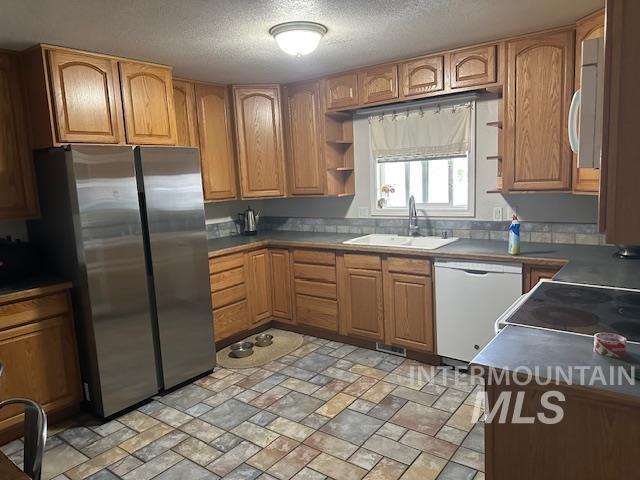 Kitchen with dark countertops, brown cabinetry, freestanding refrigerator, white dishwasher, and a textured ceiling