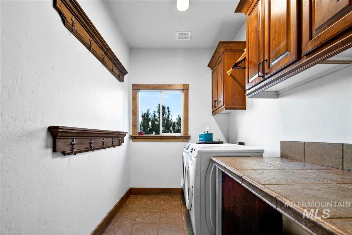 Dedicated laundry area featuring a tile countertop, wood-finish cabinetry, built-in hanging rack, two wall-mounted coat racks, and a window with wood trim