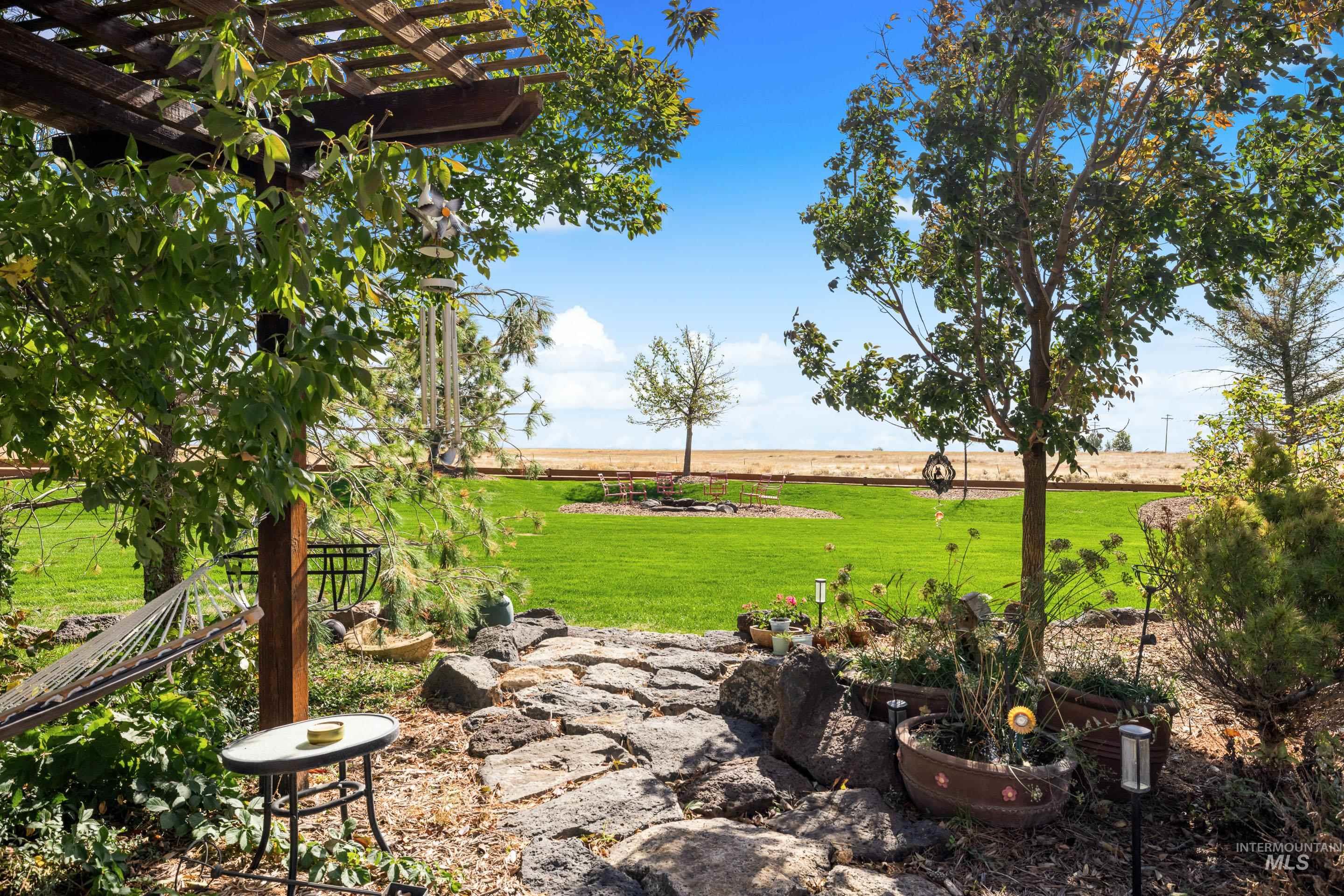 Expansive backyard featuring a stone pathway, a lush green lawn, mature trees, and a wooden pergola