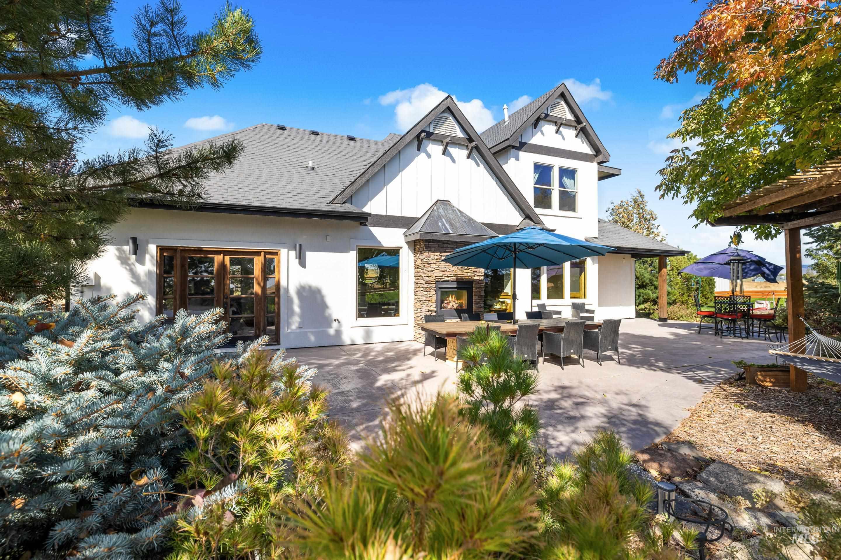 Spacious rear patio featuring an exterior fireplace with stone surround, double wood-frame glass doors, and a covered pergola